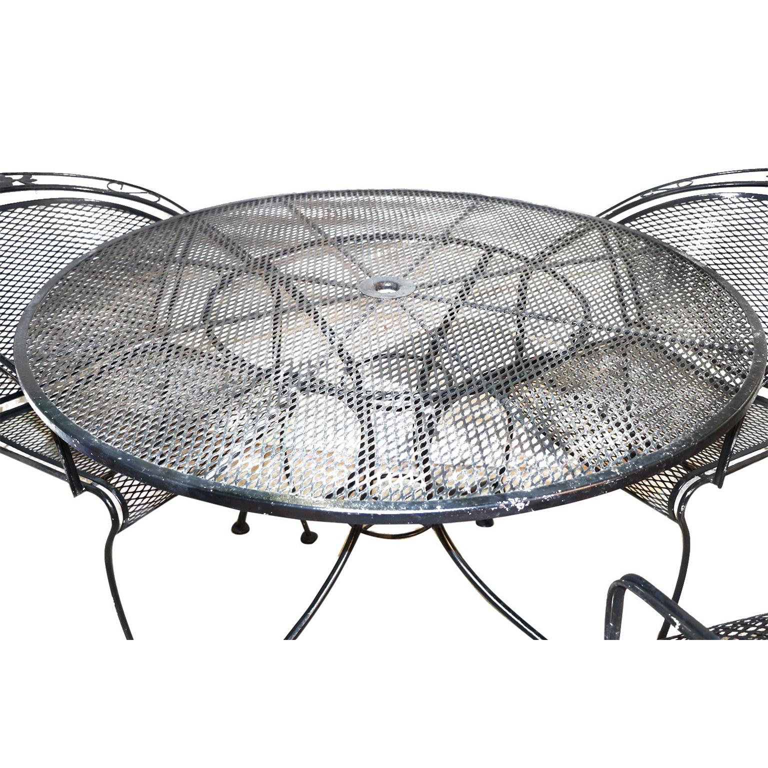 Fantastic Mid-Century Modern five-piece wrought iron garden or patio set, in the style of Russell Woodard, USA, circa 1950s. This lovely black iron set includes a circular dining table and four armchairs. The dining table features a metal mesh top