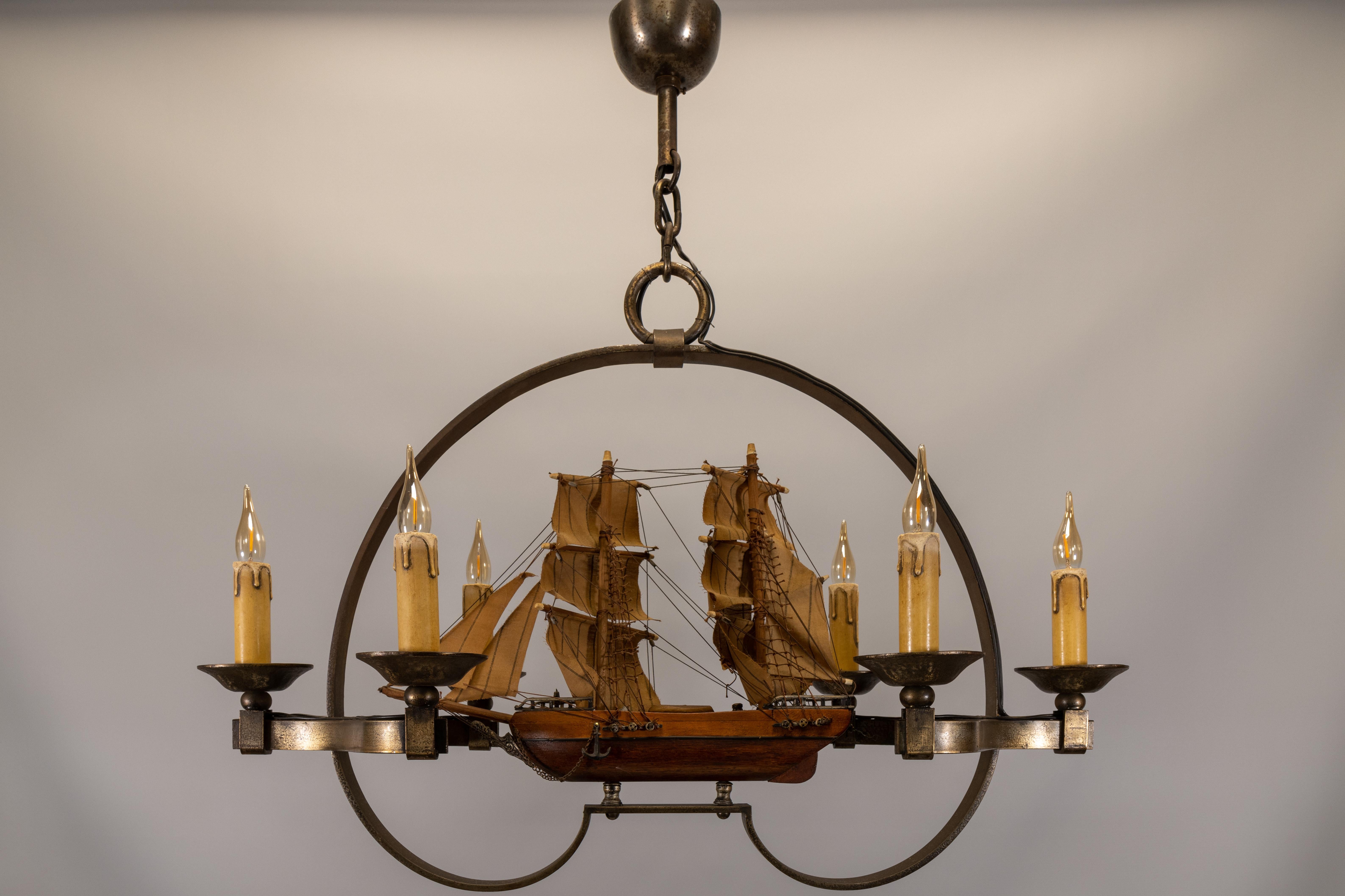 Ein seltener französischer Kronleuchter aus den 1970er Jahren mit einem handgefertigten Holzschiff, das von sechs schmiedeeisernen Kerzenlichtern umgeben ist. Dieses einzigartige Einzelstück verbindet maritimen Charme mit dem Charakter der
