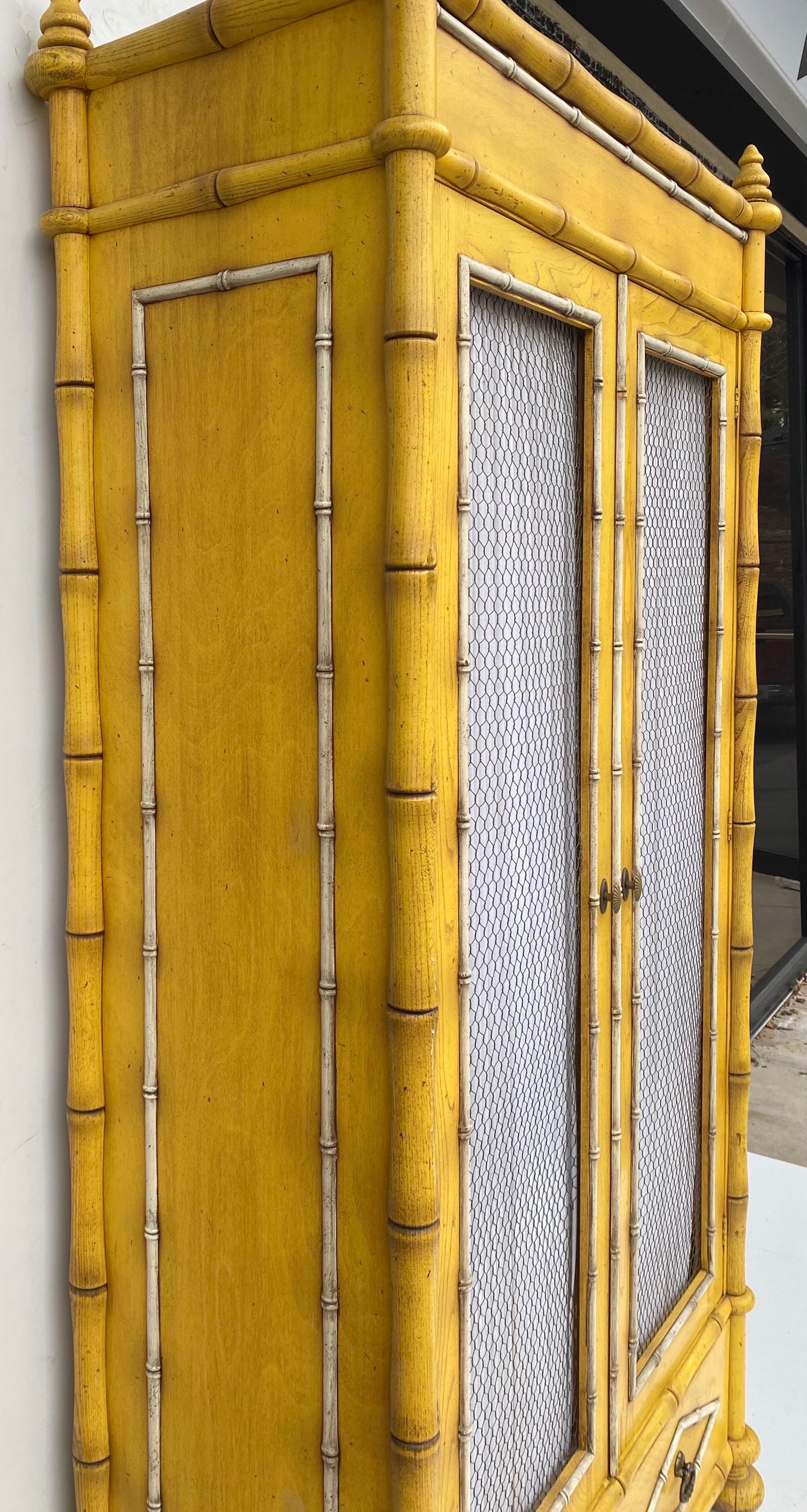 Love this! This is a midcentury yellow faux bamboo armoire with French styling. It is the original finish, and the doors are lined with both wire and fabric. It opens to nice storage and is in very good condition.