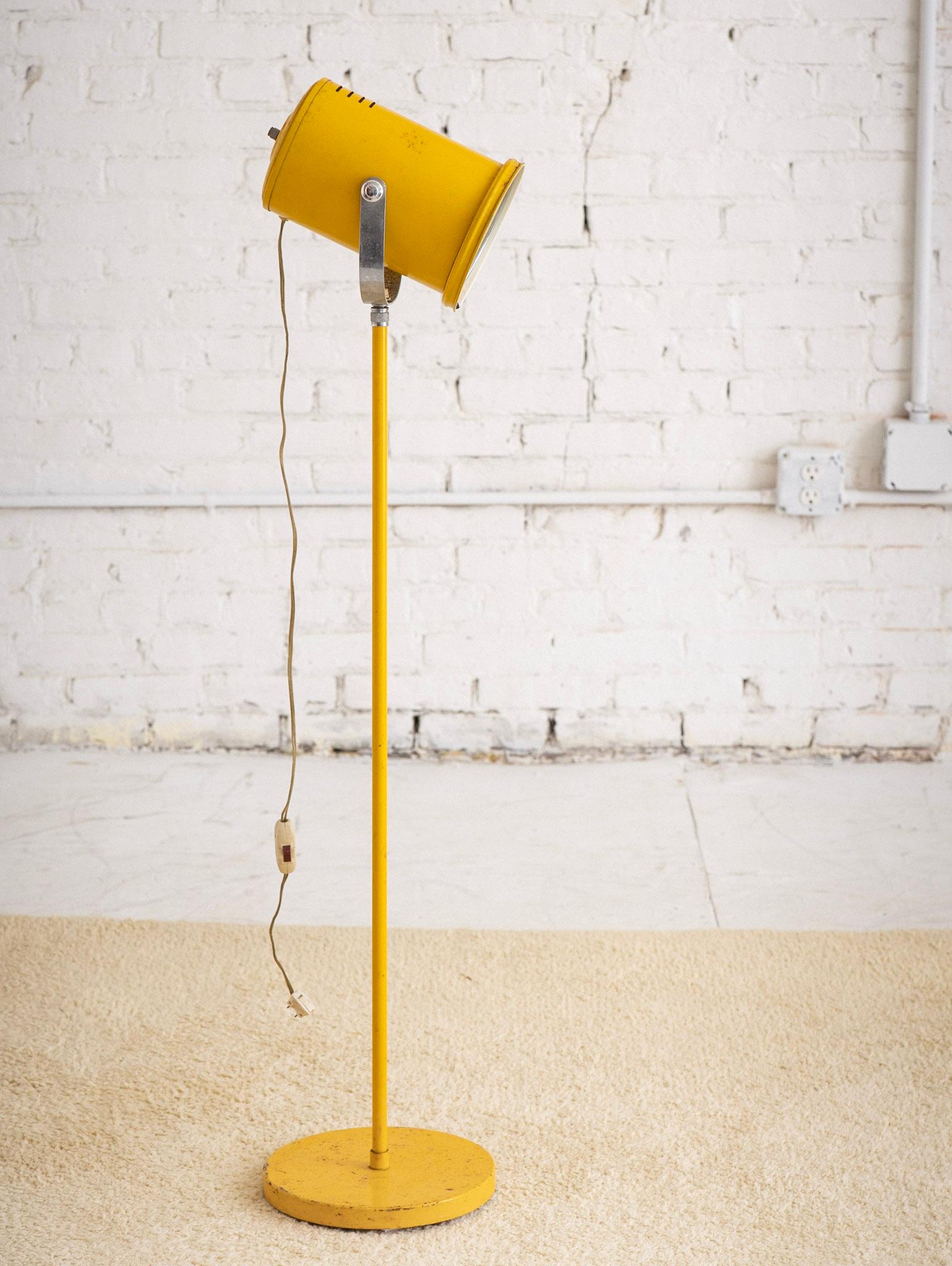 Mid Century industrial floor lamp. Original yellow coating has developed a heavy patina. Upper canister features a glass shade held in place by a tension support. Canister can be adjusted to point at desired direction. Note the current cord is quite