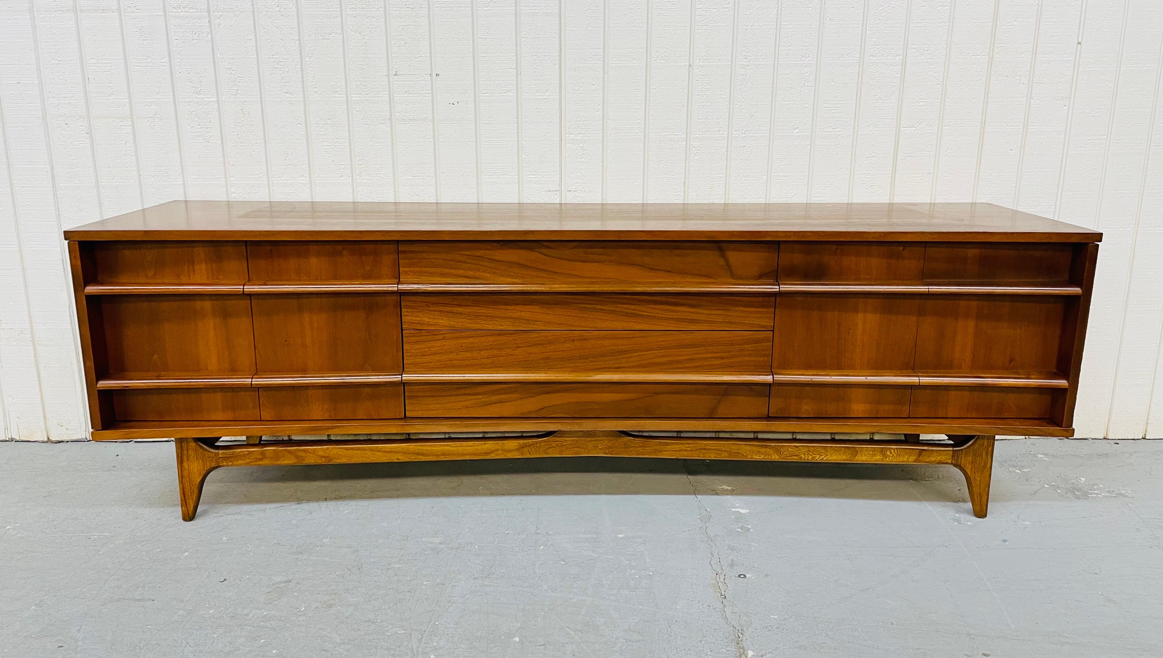 This listing is for a Mid-Century Young Manufacturing Curved Walnut Sideboard. Featuring folding doors that open up on each end to storage space, two drawers in the center, sculpted stretcher across the front, and a beautiful walnut finish.