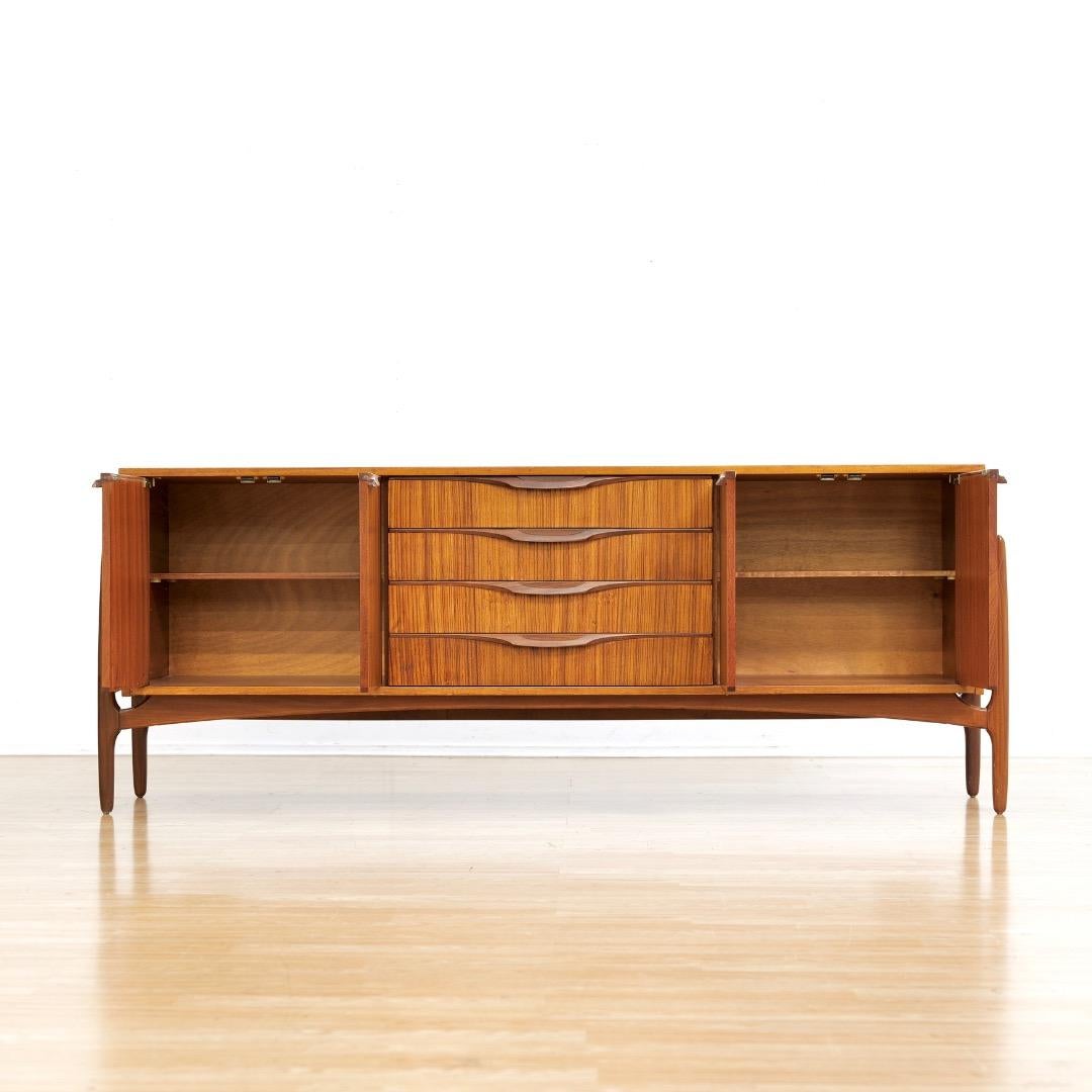 Questa straordinaria credenza è stata progettata e prodotta da 'Elliots of Newbury' del Berkshire, in Inghilterra, negli anni '60. Un meraviglioso design di metà secolo e un eccellente mobile contenitore, un esempio straordinario che sarebbe un