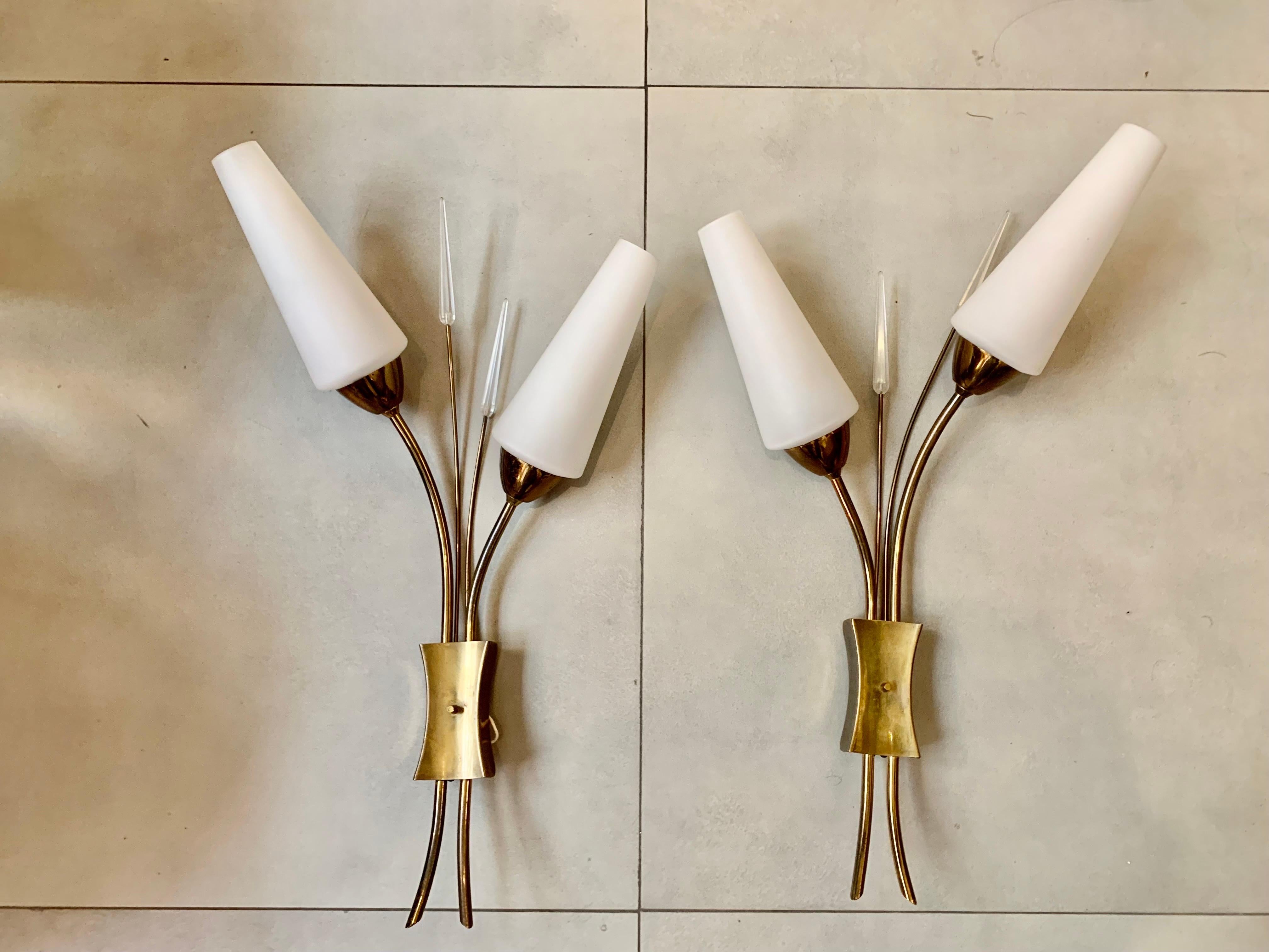 Pair of 1950s wall sconces, design Maison Lunel, France, they are double sconces, in brass metal, with glass trim, and white opaline lampshades. Prepared for electrical operation in the USA.