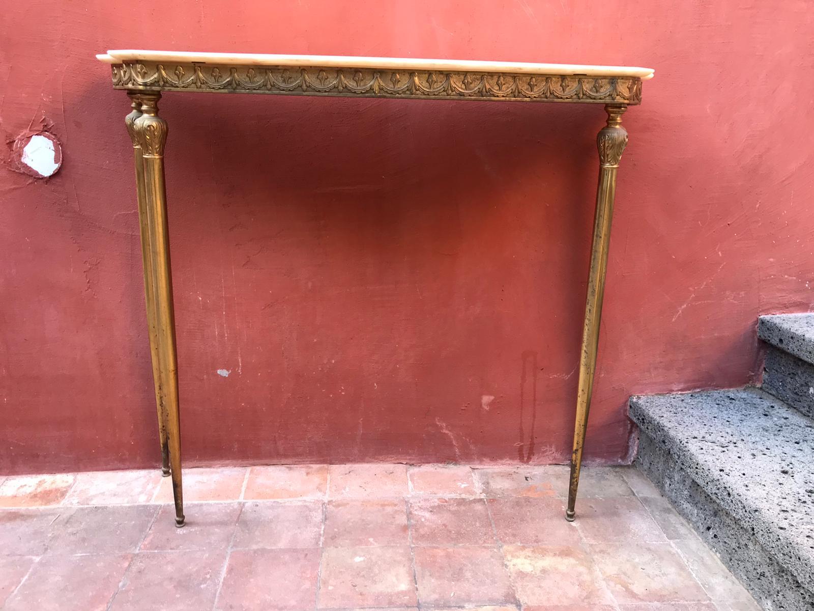 A brass console table with decorated motifs and white marble top.