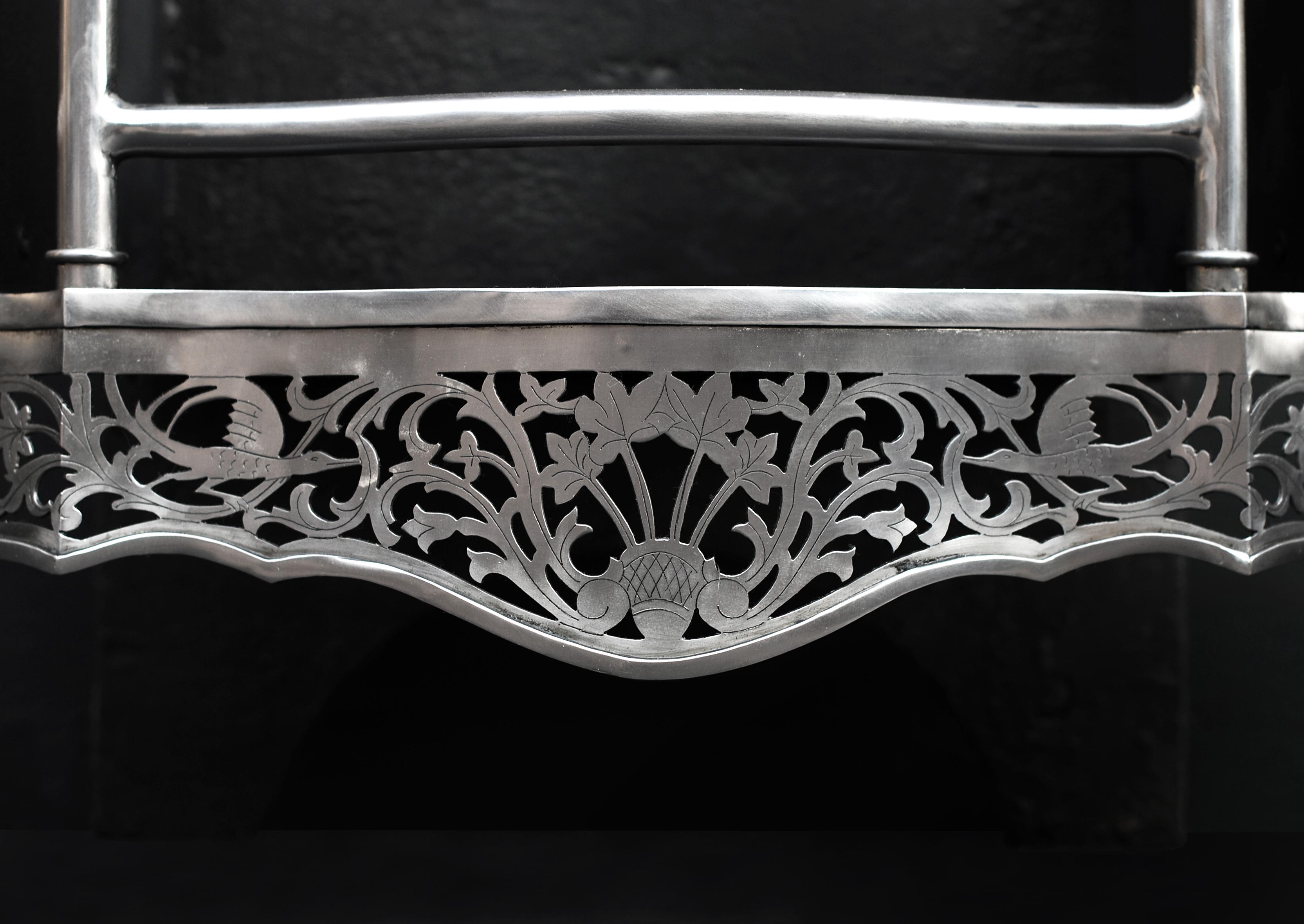 A mid-Georgian Chippendale style steel firegrate. The shaped, pierced and engraved fret with centre basket of foliage and winged heraldic birds, with columns and finials above and bowed connecting front bars. The legs with four narrow tapered