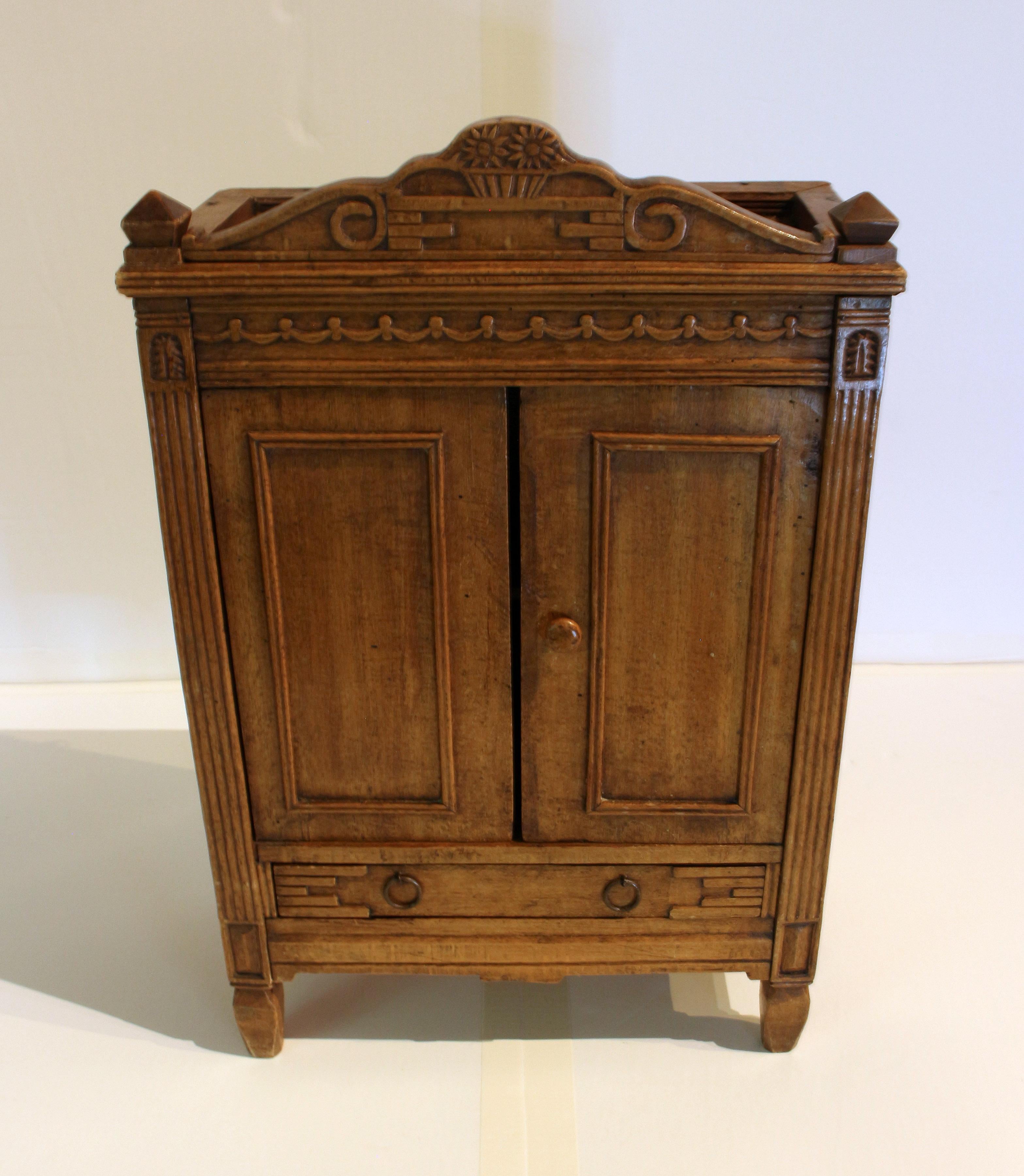 Mid-late 19th century miniature armoire, country French. Charming example, wired at the back to hang or to set on another piece. Cherry & poplar woods. Shaped crest carved with sunflowers in a basket, carved pilasters flank the doors (each now