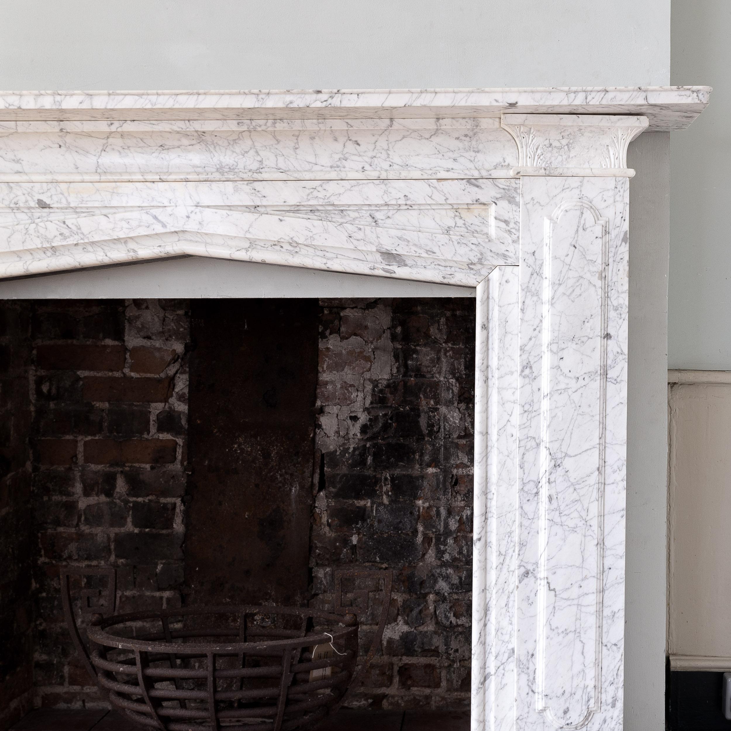 A mid-nineteenth century Old English marble fireplace, circa 1850, the lipped shelf with deep concave under-mould above panelled frieze forming a gothic arch to the aperture, the pilaster jambs to either side with raised elongated lozenge panels