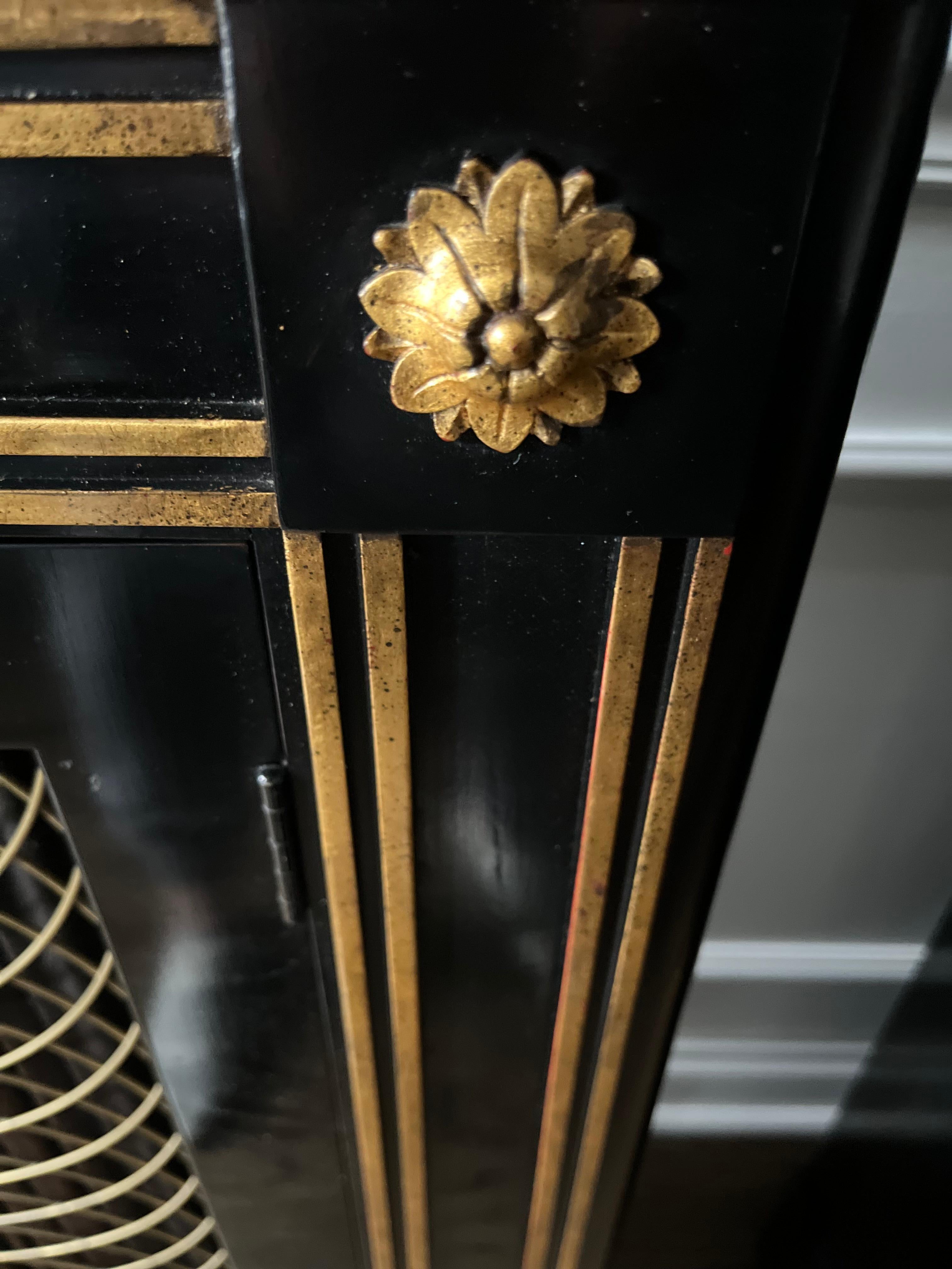 An ebonized and gilt two door/two shelf cabinet in the Regence style. A perfect cabinet for a narrow space in the style of Maison Jansen having gilt rosettes and a grille backed by a black linen. Another possible attribution could be to Mario Buatta