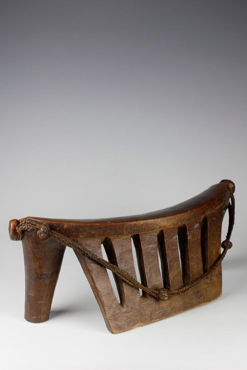 Ce grand appui-tête du milieu du XXe siècle, sculpté dans une seule pièce de bois, provient de la culture Dinka du Sud-Soudan. Avec de multiples supports verticaux, l'appui-tête affiche une merveilleuse forme animale. 

Une sangle en cuir tressé,