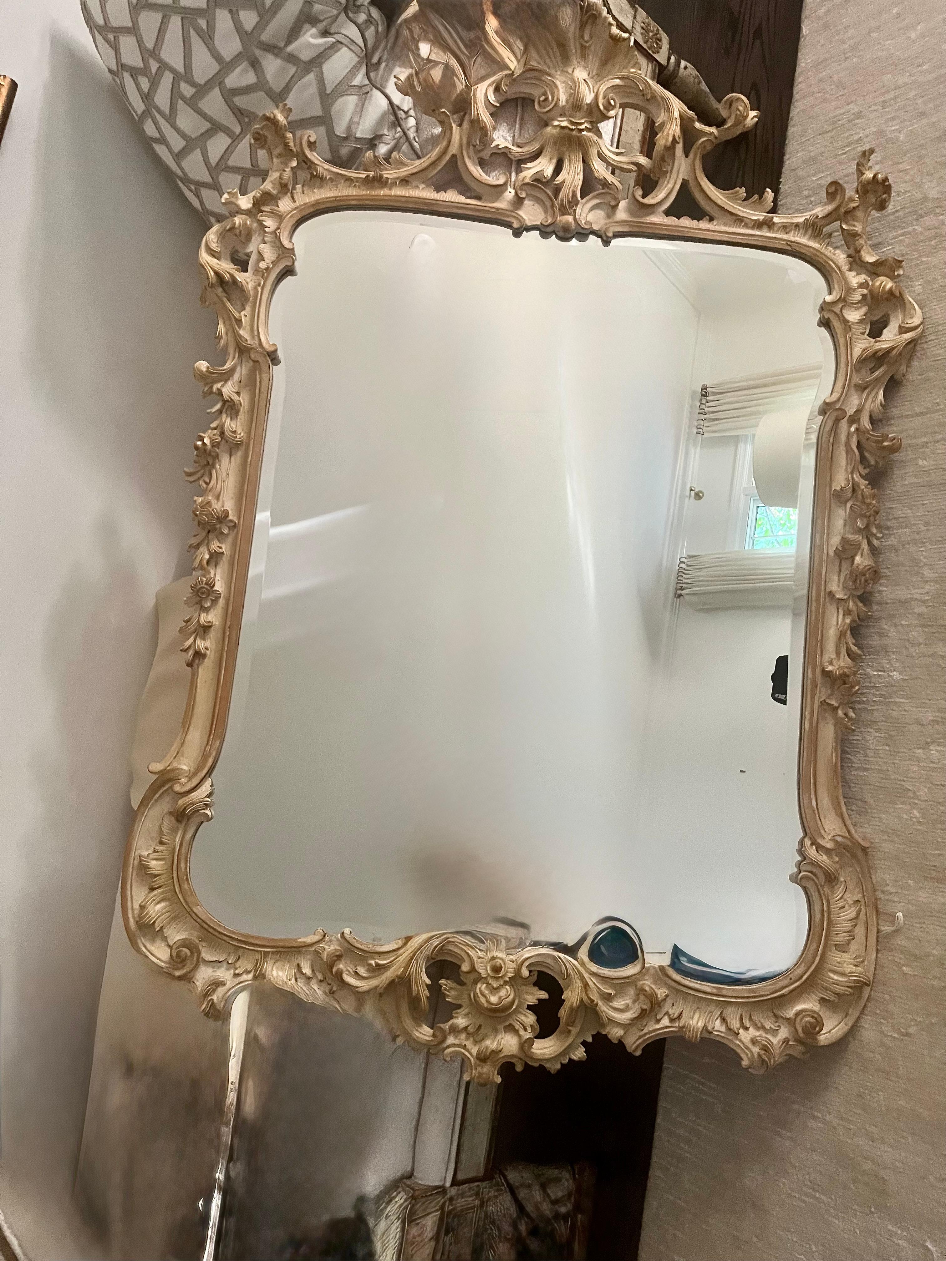 A Mid Twentieth Century Rococo style beveled mirror by La Barge, having an elaborate overall  carved frame with a shell crown, foliate and floral carvings having gilt paint undertones making it adaptable to today's more relaxed decor. 
