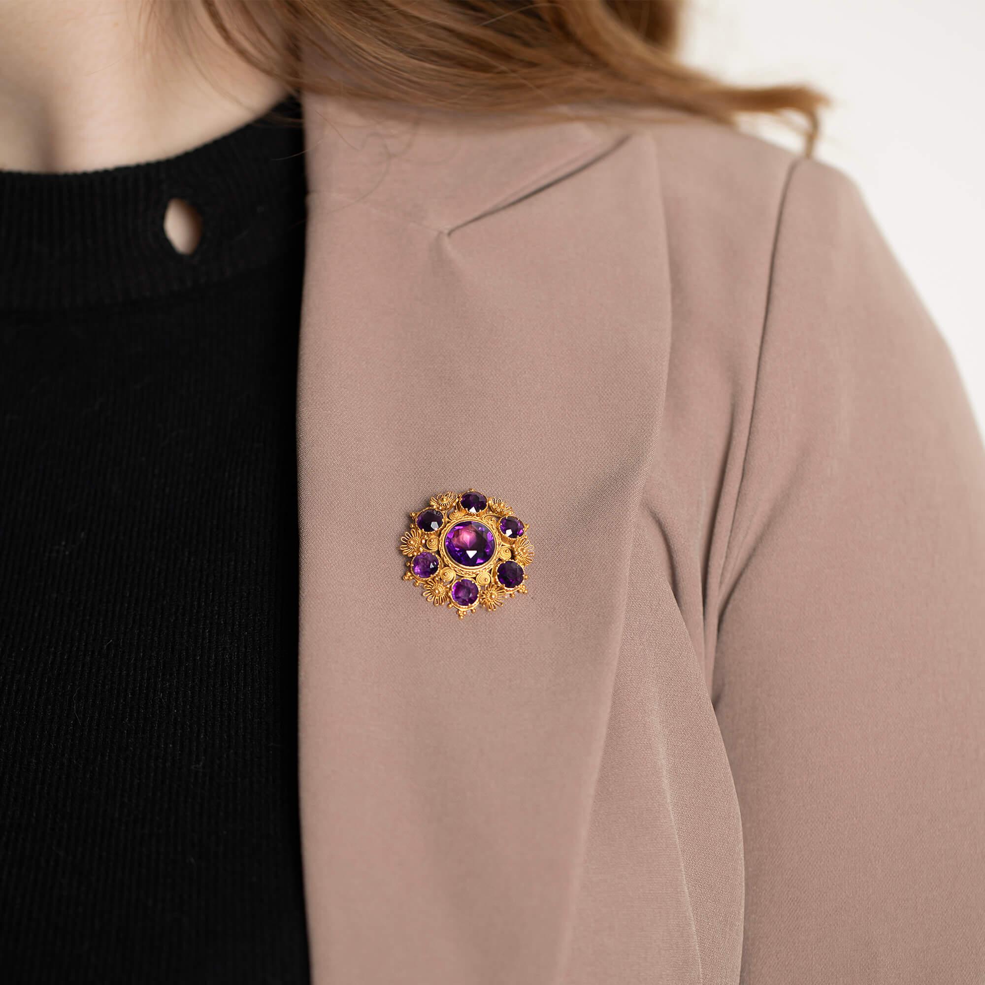 A superb Mid-Victorian circular brooch with fine cannetille and bead wire work forming swirls and flowers. Secured and fitted with a pin and hook catch.

Gemstone: One 12mm round and six 6mm natural amethysts, good mid-purple material
Metal: 18k