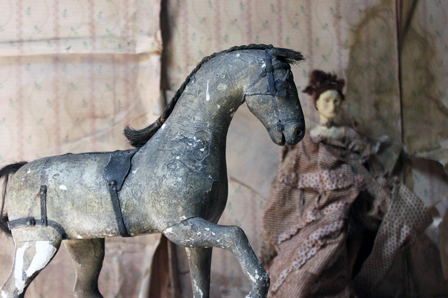 The decorative child's Victorian dappled carved and painted wooden pull-a-long horse, with one front leg raised, having a black leather saddle and harness, plaited horse-hare and mane, to a black painted base and four wheels, surviving in un-touched