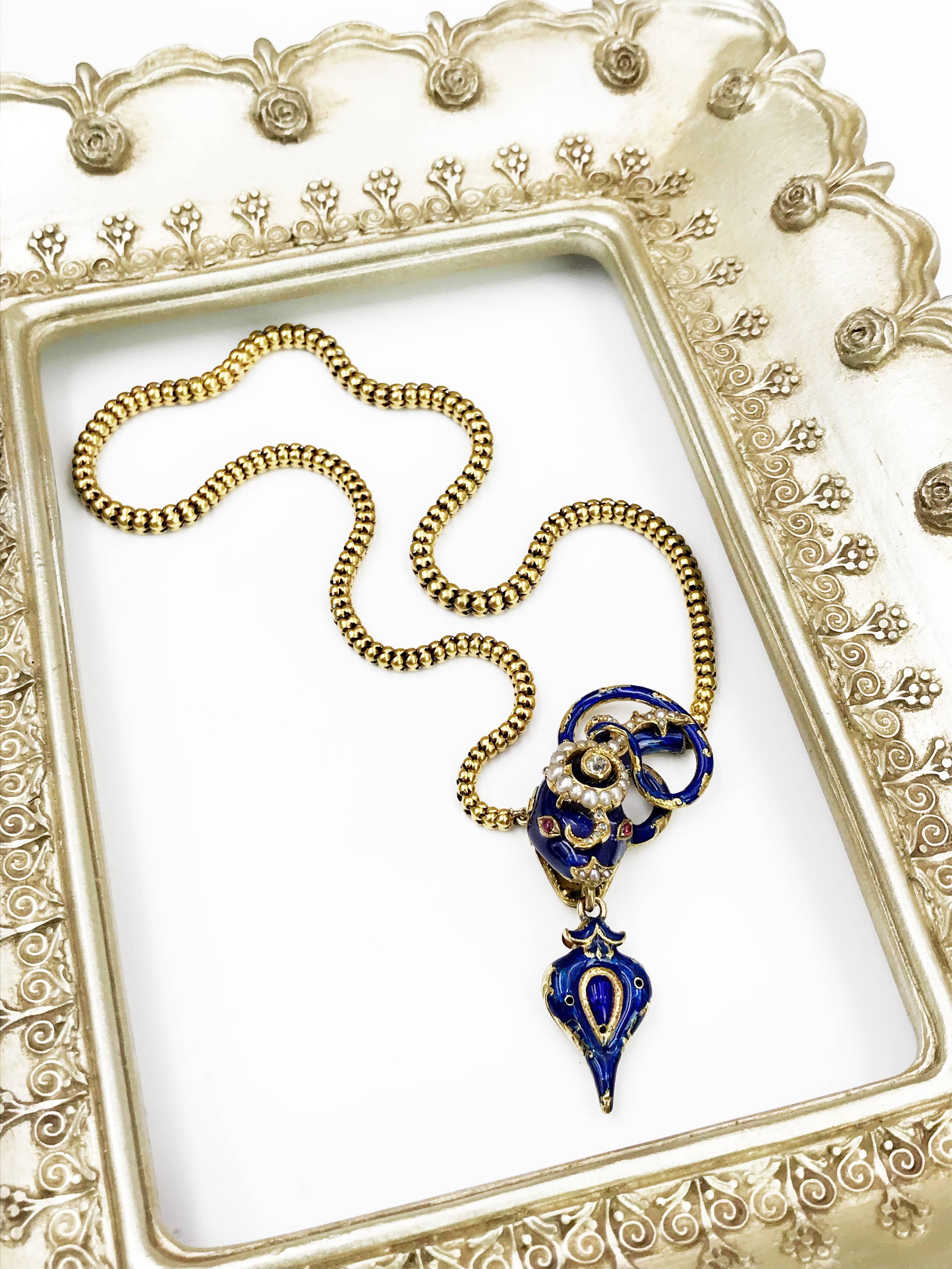A mid Victorian 20ct/ 22ct gold, enamel and gem-set snake necklace. The blue enamel head and scrolling tail, with ruby cabochon eyes and vari-cut diamond and split pearl crest, suspending a blue enamel heart locket, to the snake-link chain.
