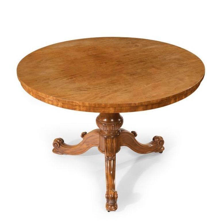 A mid-Victorian faded satinwood centre table, attributed to Holland and Sons, the circular top set on a baluster support with three scroll-ended cabriole legs, original castors, English, circa 1860.