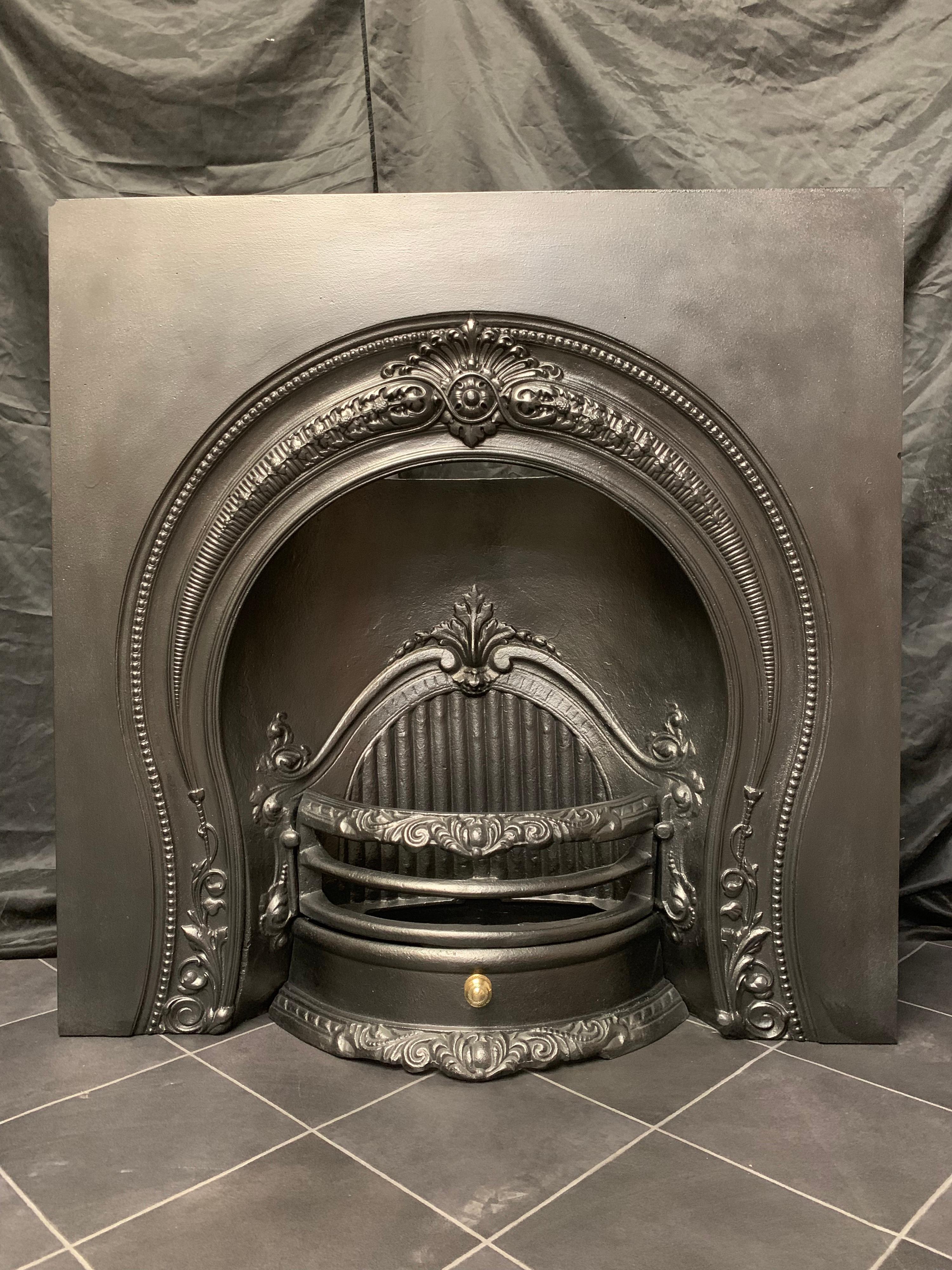 A generous sized Mid Victorian Horseshoe style arched cast iron fireplace insert, a large outer plate with a decorative central cartouche with curved horns following the contour of the horseshoe opening, the internal curved fire back with reeded