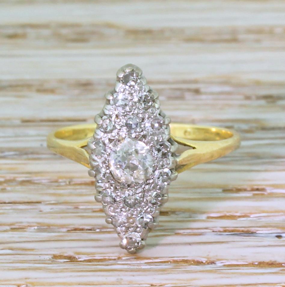 An ideally proportioned vintage navette ring. At the heart of the ring is a white and bright old cut diamond of just under a third of a carat, with sixteen smaller eight-cut diamonds in a white gold coronet setting. On a slim and tapering yellow