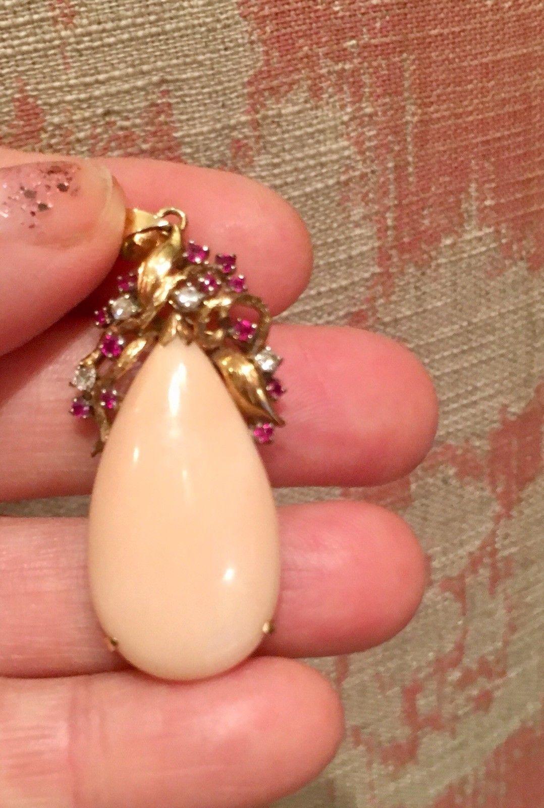 Stunning pear shaped angel skin coral cabochon is sent in a 14k gold surround with a pendant loop at the top and striking ruby and diamond gemstones. What a gorgeous soft colored pendant with beautiful pinks and reds! 

The red ruby faceted