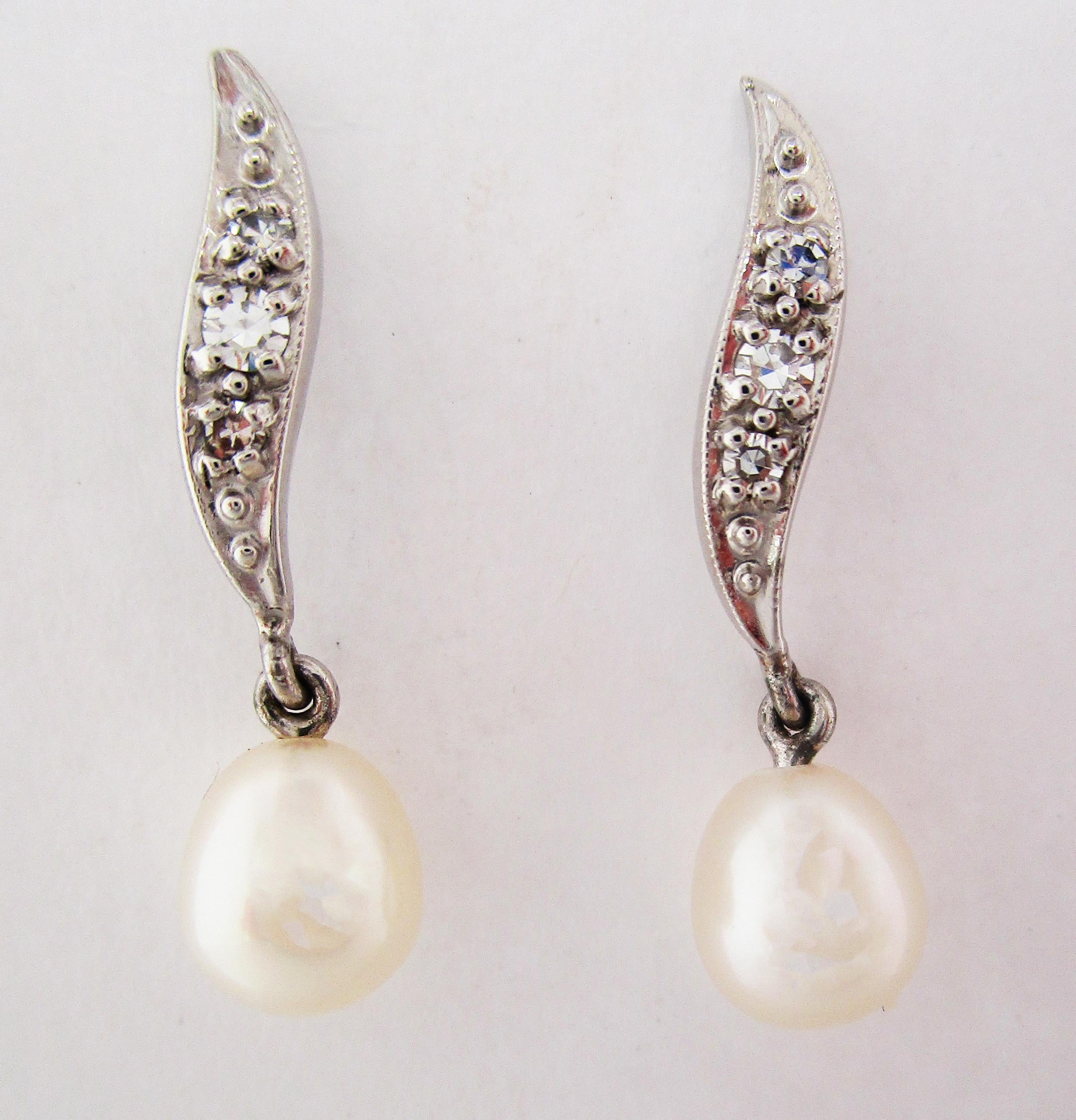 These elegant mid-century earrings are in bright 14k white gold and feature a curved top portion set with three diamonds and finished by an articulated pearl drop. The style of these earrings defines the 40s and 50s. The combination of white gold,