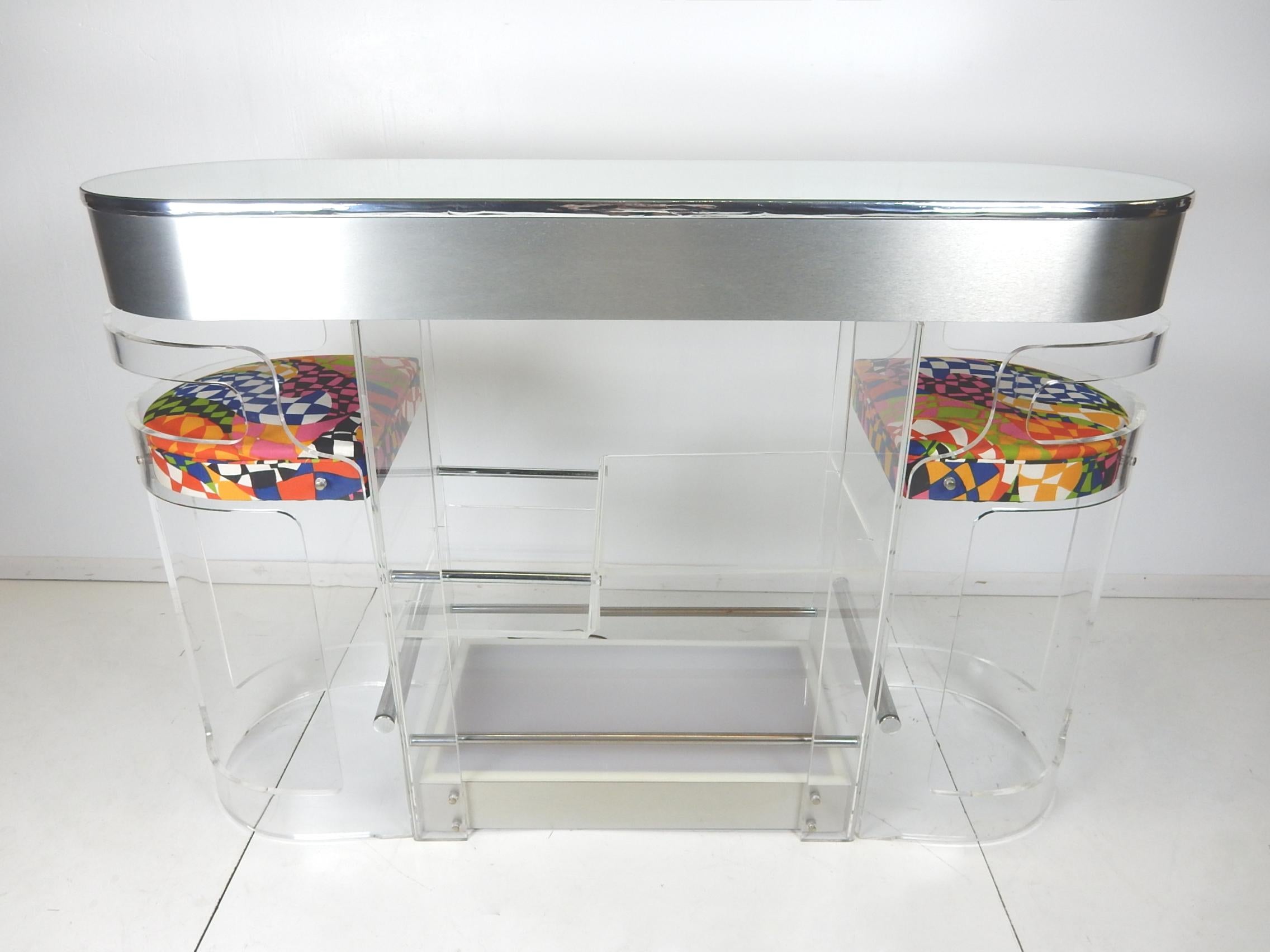 Mirror top Lucite bar with two matching stools by Hill Manufacturing, circa 1970s
Multi level shelf's, supported by chrome rods, for storing mixology needs. Eight bottle storage slots on the bar tenders side.
Two stools tuck neatly in on either