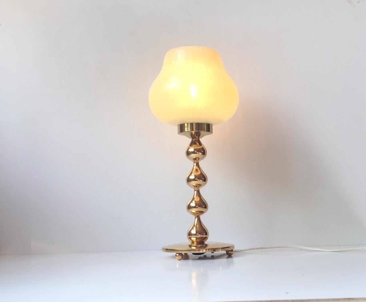 24-carat gold-plated table light composed of four intervened drops. It is mounted with a pin-stripe pastel glass shade. It was designed during the 1960s by Hugo Asmussen in Denmark. The base/foot of the light shows ware and patina due to patination