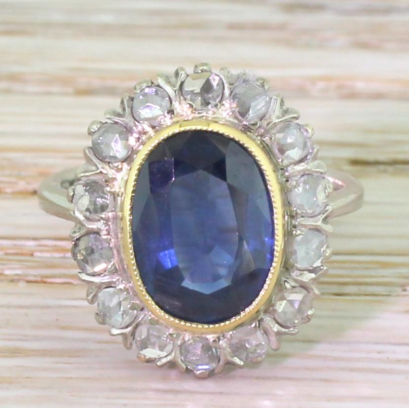 
A super pretty sapphire and rose cut diamond coronet cluster. The vibrant, bright blue sapphire is rubover set in milgrained yellow gold, and is surrounded by fourteen rose cut diamonds. The beautifully and finely pierced white gold gallery leads