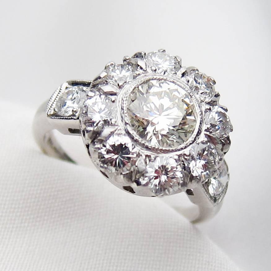 Circa 1950. This magnificent midcentury platinum ring features a central, round brilliant-cut diamond weighing 1.14 carats, with a VS1 clarity and M color. Clustered around the central stone are eight round brilliant-cut diamonds. One brilliant-cut