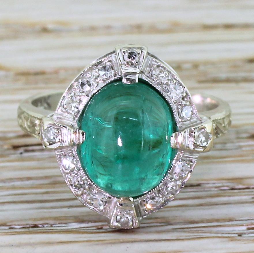 A high class emerald in a showstopper of a mount. The Colombian emerald in the centre displays a bright and glowing bluish green, and is surrounded by sixteen eight-cut diamond – including four in the raised claws. The simple double gallery leads to