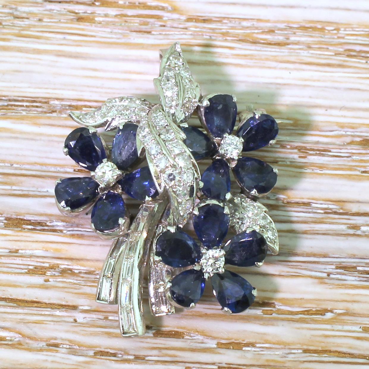 A highly impressive sapphire and diamond brooch. Comprised of three flowers with five pear cut sapphire “petals” around a brilliant cut diamond bud, with four beautifully shaped diamond set leaves in the interweaved, and three baguette cut diamond