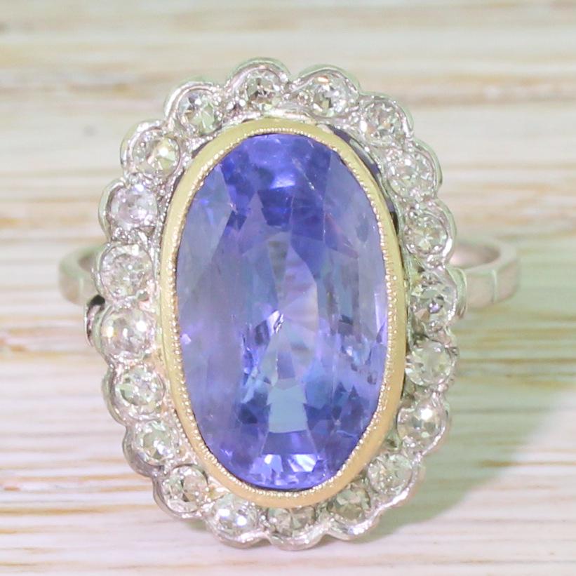 A glorious cornflower blue natural and unheated sapphire from Ceylon. The glowing stone is secured in yellow gold milgrained rubover setting, with twenty eight-cut diamonds rubover set in the surround. Fine keyhole-shaped detailing in the