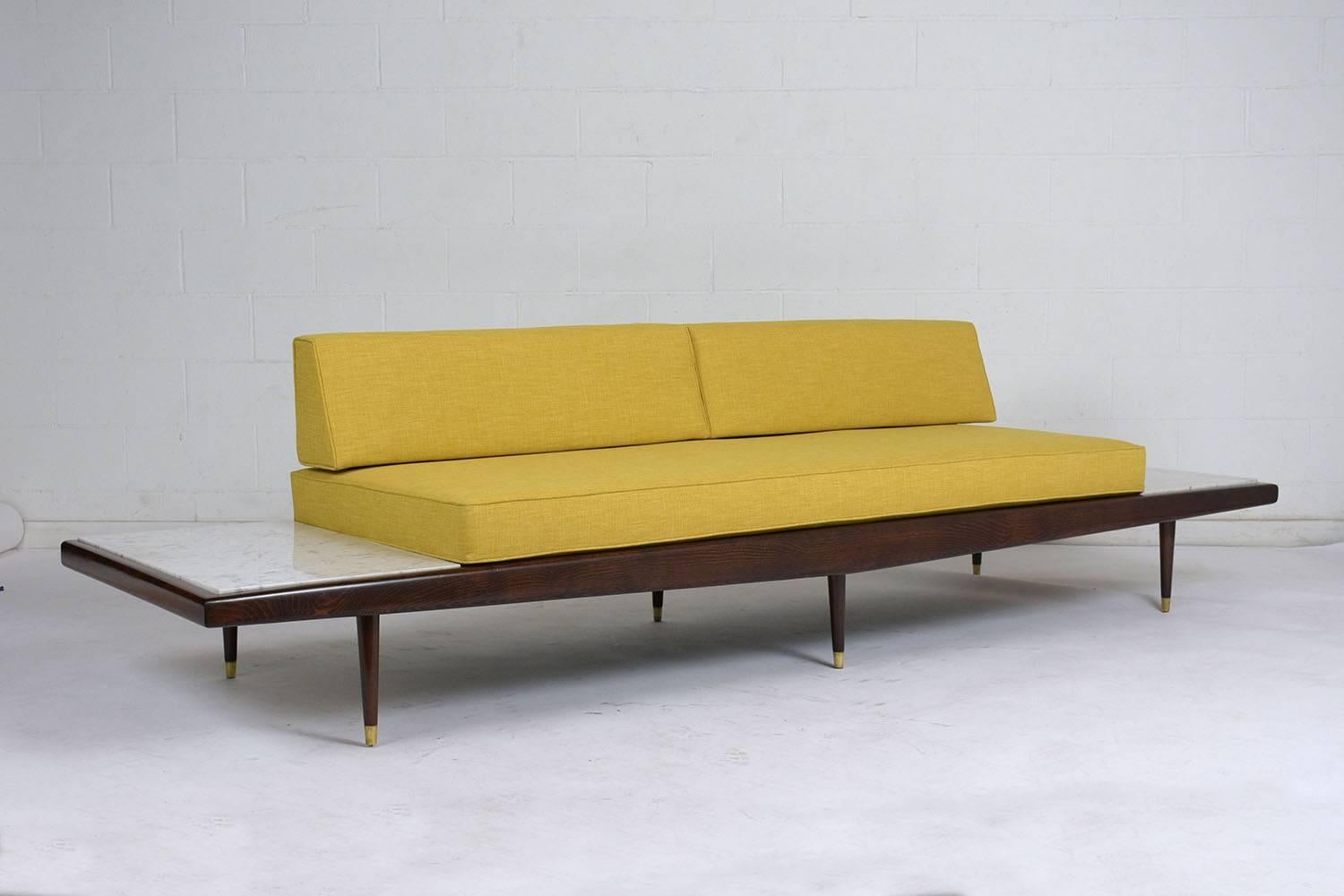 This 1960s Mid-Century Modern sofa is designed by Adrian Pearsall for Craft Associates. The boomerang style wood frame is stained a rich walnut color with a lacquered finish. Extending from the ends of the cushion are built in side tables with