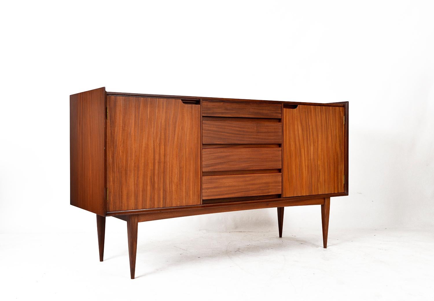 This delightful sideboard was designed by Richard Hornby for Fyne Ladye Furniture during the 1960s. The piece provides ample storage space with its two spacious cupboards, which open to reveal adjustable shelves. The four central drawers feature