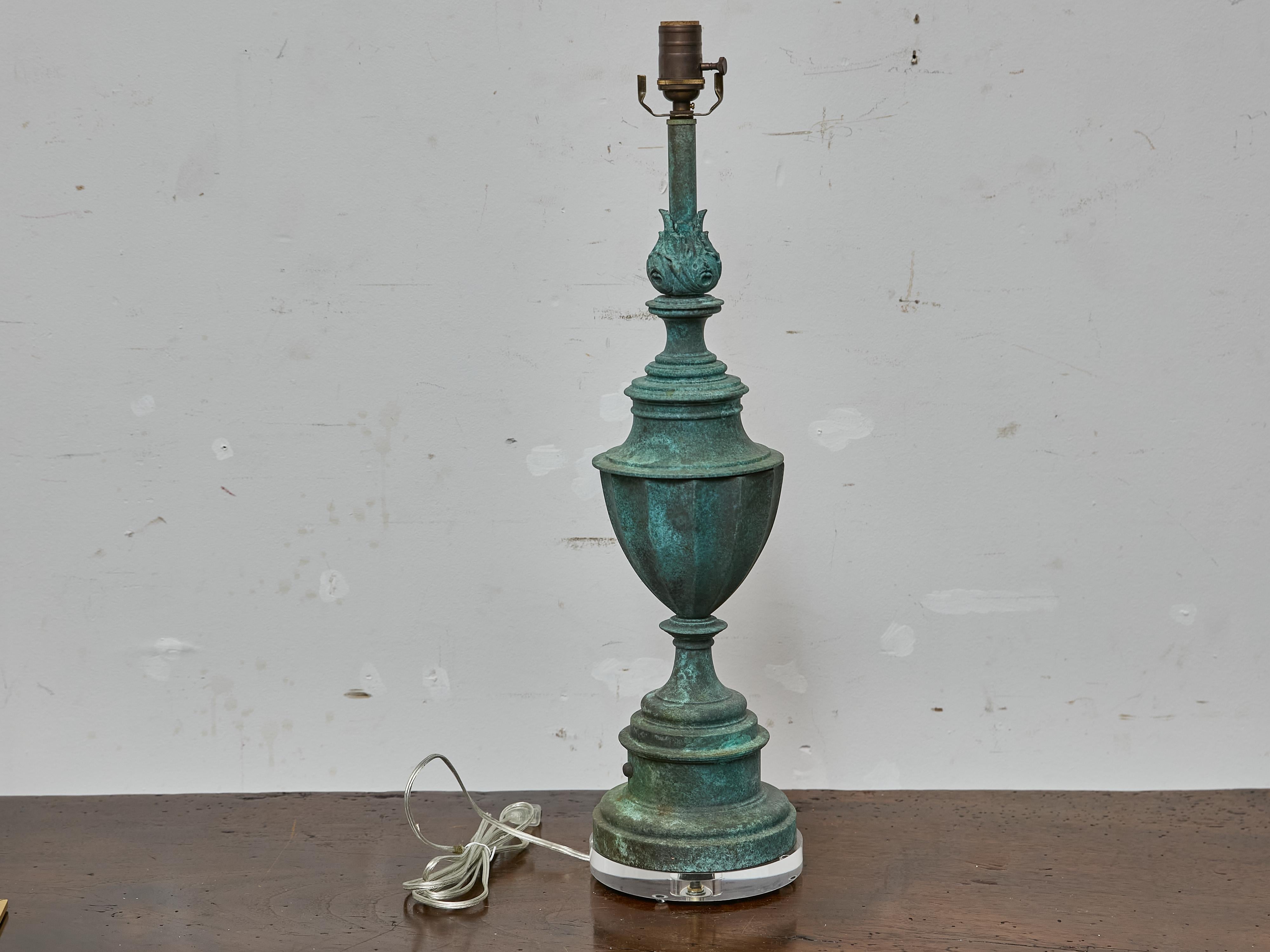 A stately Midcentury table lamp crafted in copper with a rich verdigris patina, mounted on a clear Lucite base. This American lamp features a classically inspired silhouette with a subtly faceted urn body, tiered circular base, and elongated neck