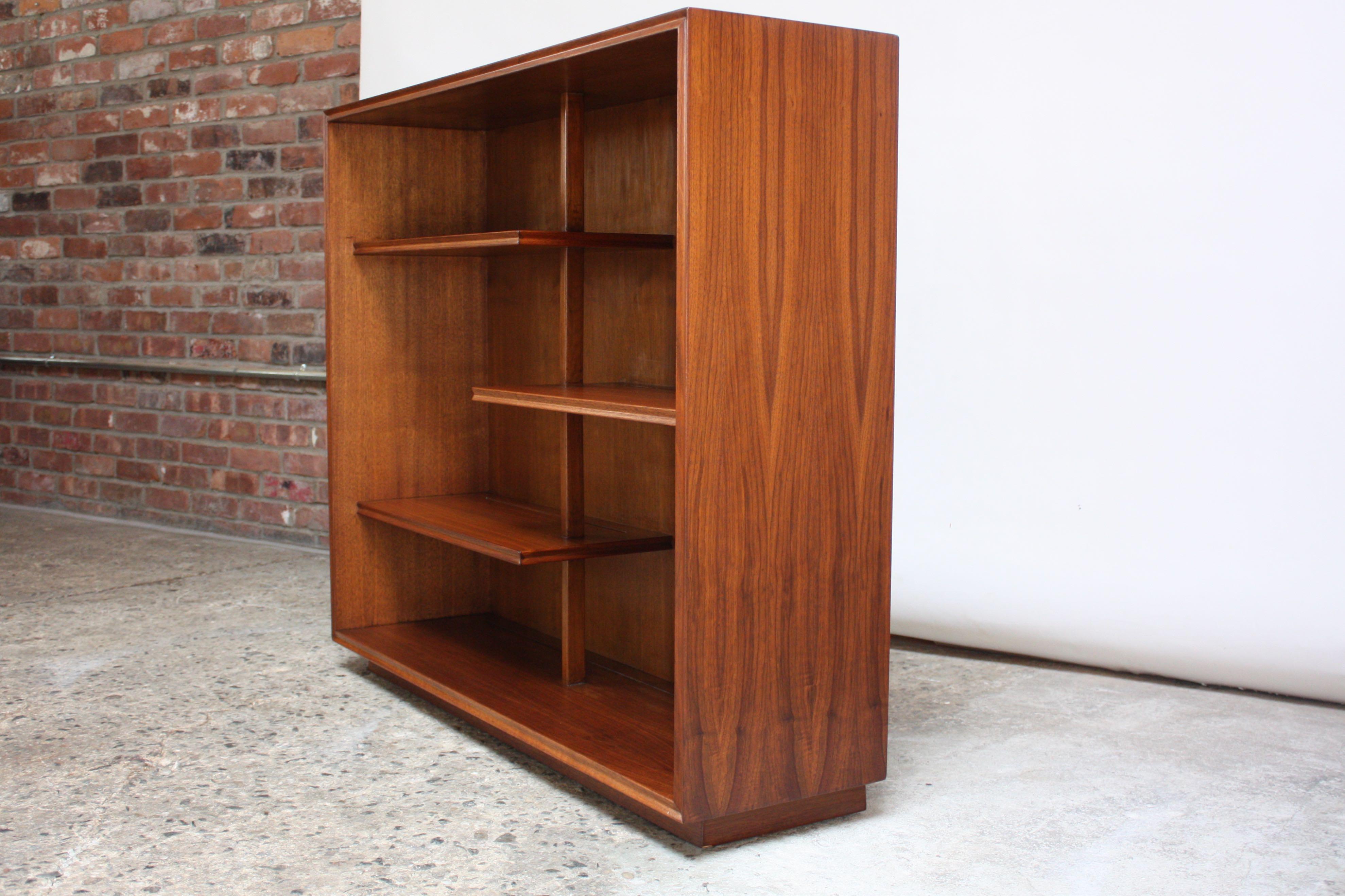 Organic-form midcentury bookcase composed of three 'floating' shelves suspended by a carved walnut support. Lower shelf (base of bookcase) serves as additional storage. There are thin, long slits carved into the back of each shelf for display