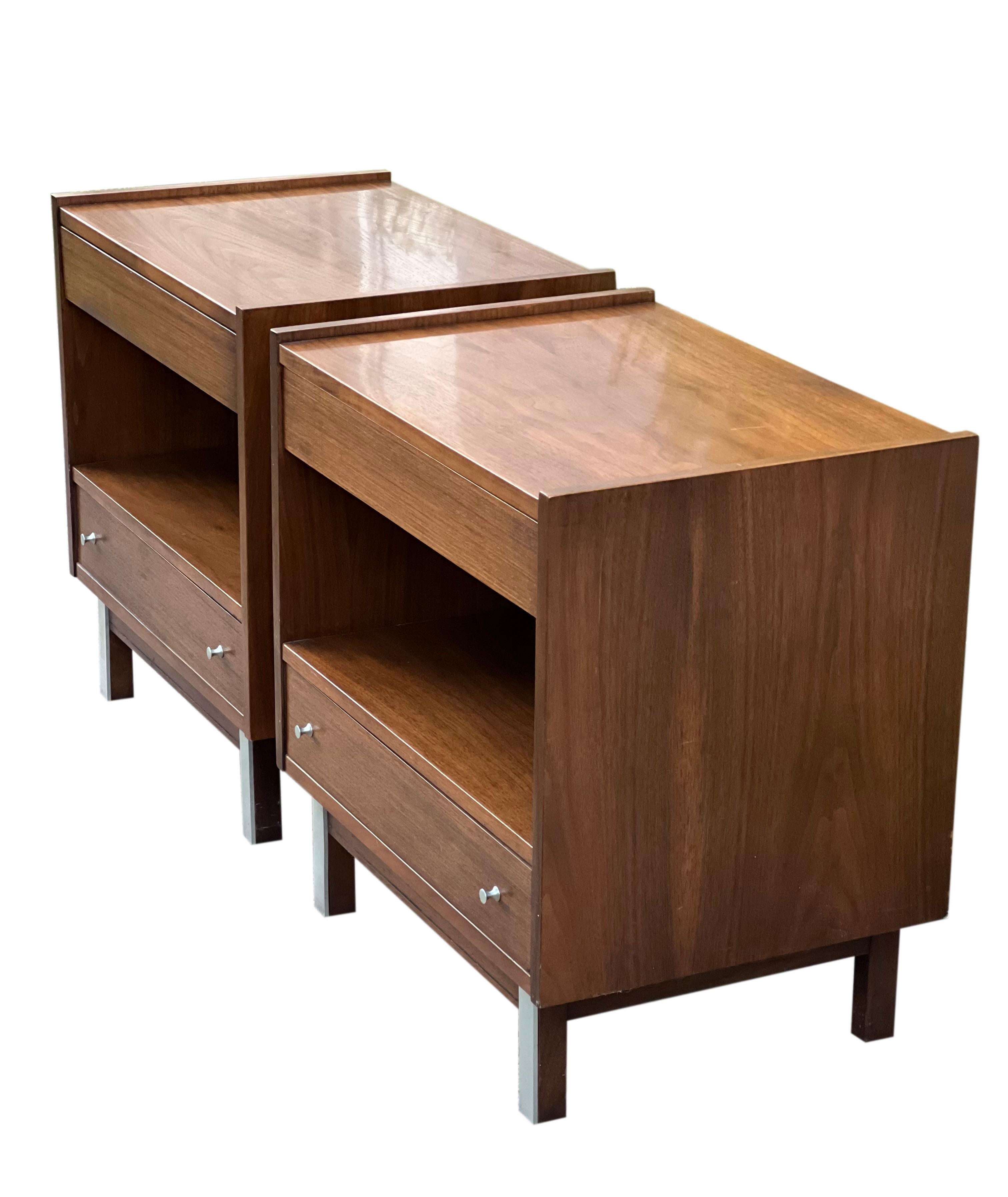 Handsome pair of 1960's walnut nightstands by American of Martinsville.

The nightstands feature a classic Midcentury Modern design and offer two drawers and open cabinetry which are both in very clean condition. Matte finish original metal knobs