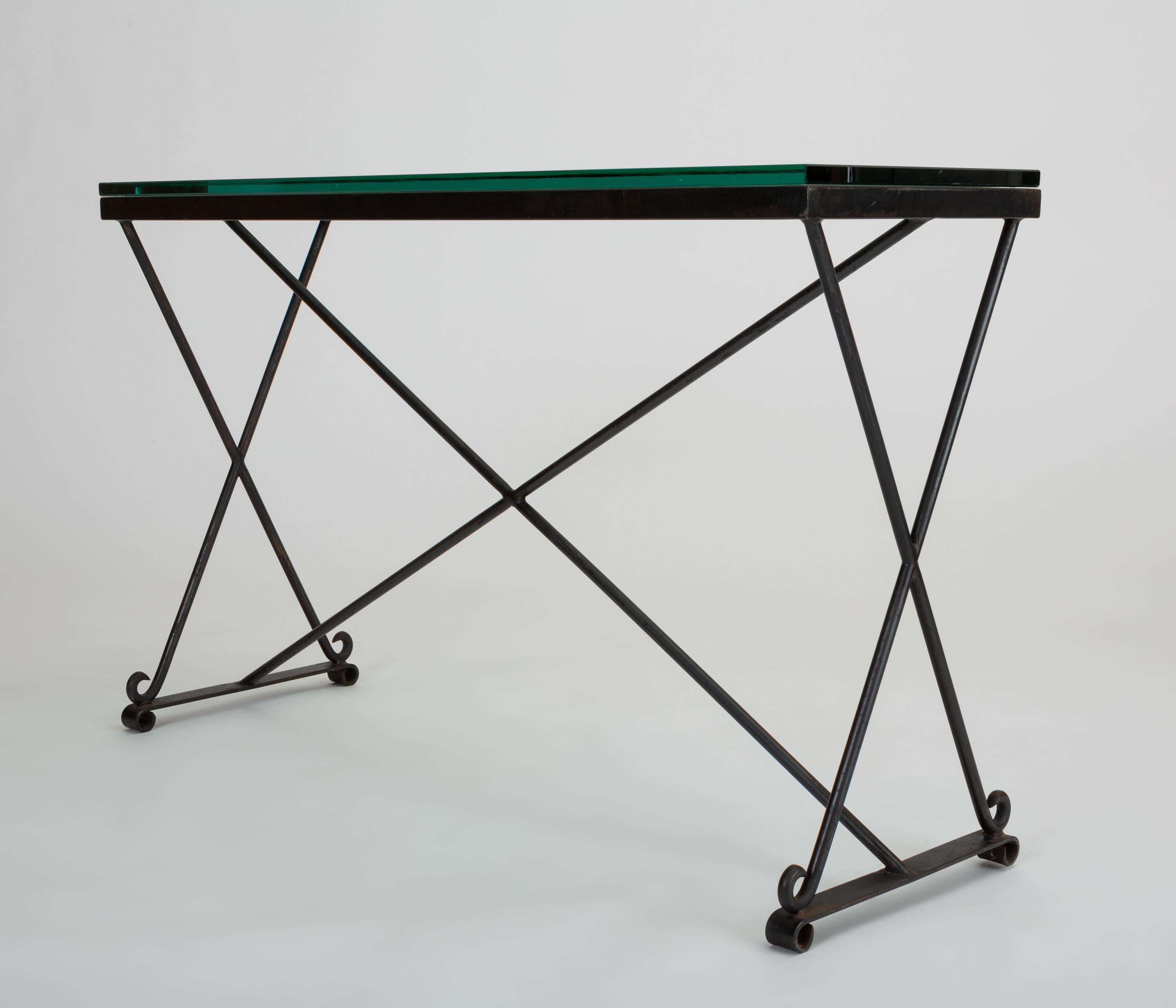 A midcentury wrought iron console table with subtle decorative elements. The versatile piece has a wire frame with trestle legs and an X-shaped center brace. Each segment terminates in a curlicue of tapered iron. The tabletop is thick-cut-glass.