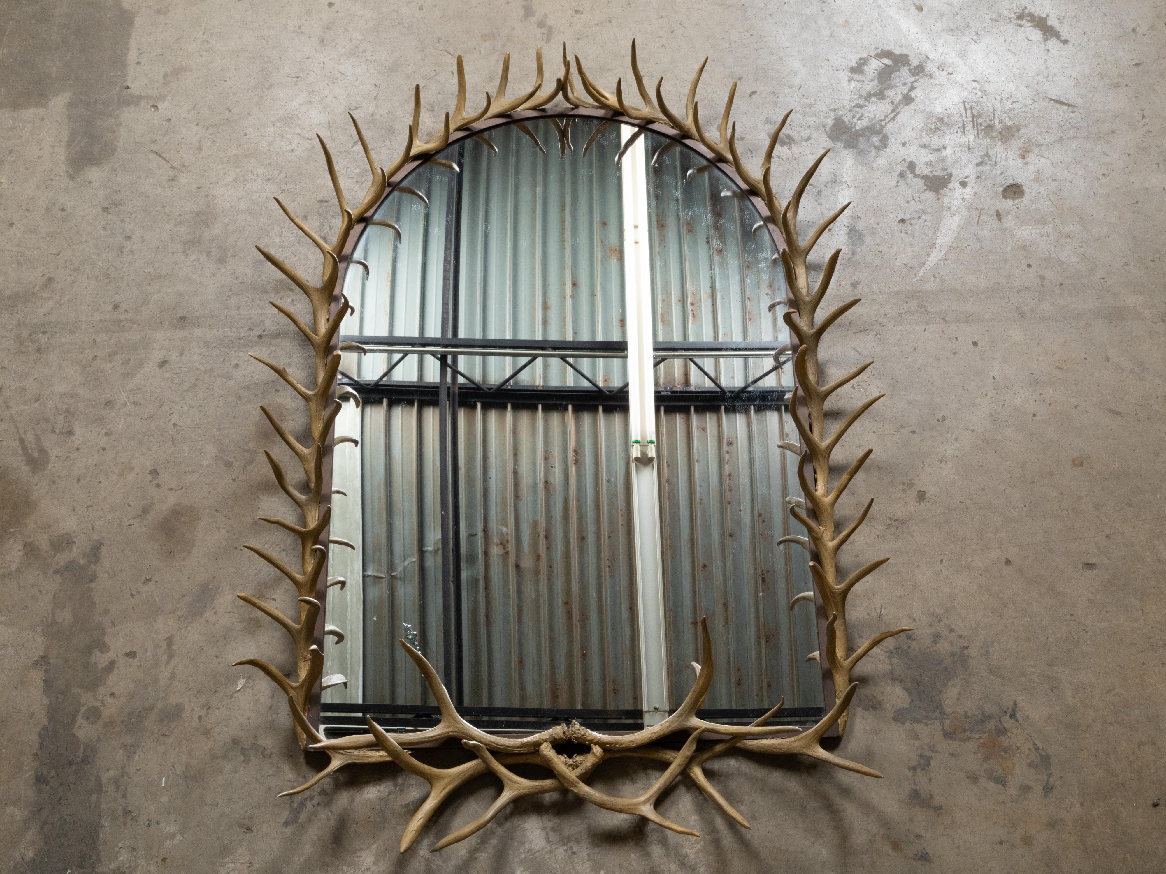 A rustic antler wall mirror from the mid 20th century with clear mirror plate and arching frame. This mid-20th century rustic antler wall mirror is an exquisite piece that combines the allure of natural materials with functional artistry. The frame,