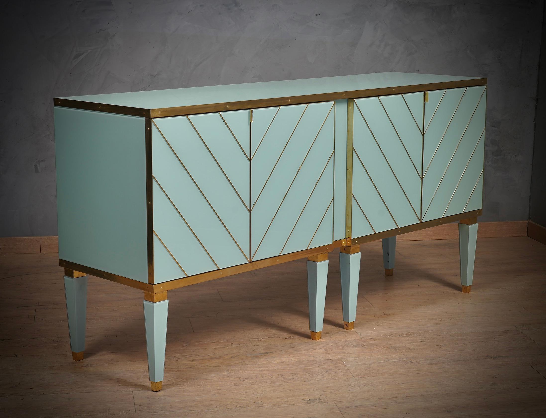 Very particular sideboard in aqua green glass beautifully finished with brass rods. Very elegant door design.

The sideboard has a wooden structure, and was externally plated with aqua green glass and then edged with polished brass finishes. Brass