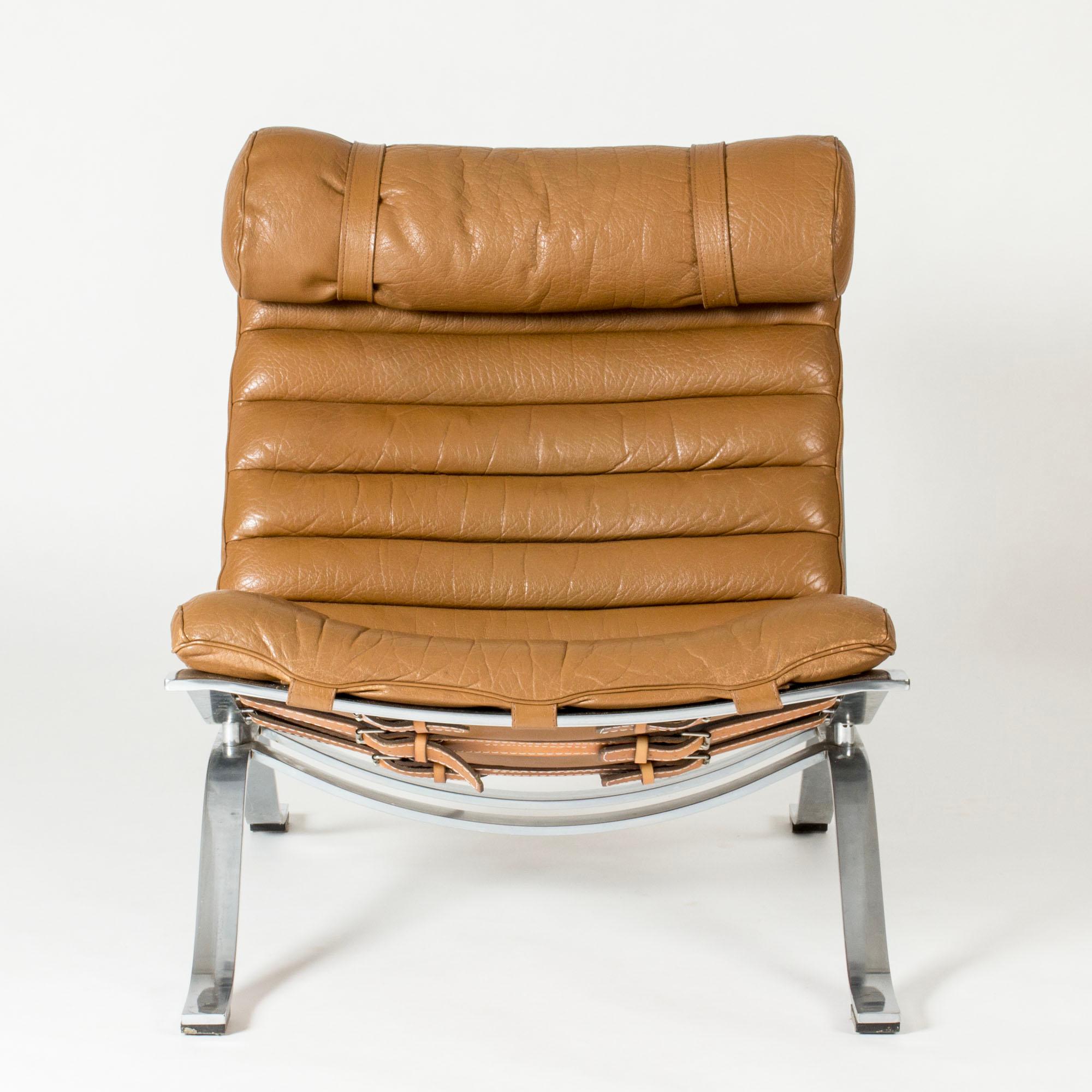Cool and comfortable “Ari” lounge chair by Arne Norell, made from steel and leather. Striking and decorative belt closing on the back. Leather in a milk chocolate brown color.
