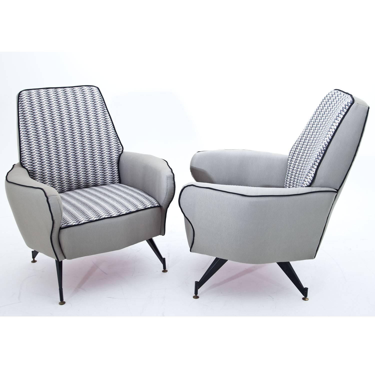 Pair of midcentury lounge chairs on black iron legs with brass feet and trapezoidal backrests. The armrests curve slightly outward. The backrests and seats are upholstered with a blue ziczac patterend fabric, the sides with an elegant grey ripped