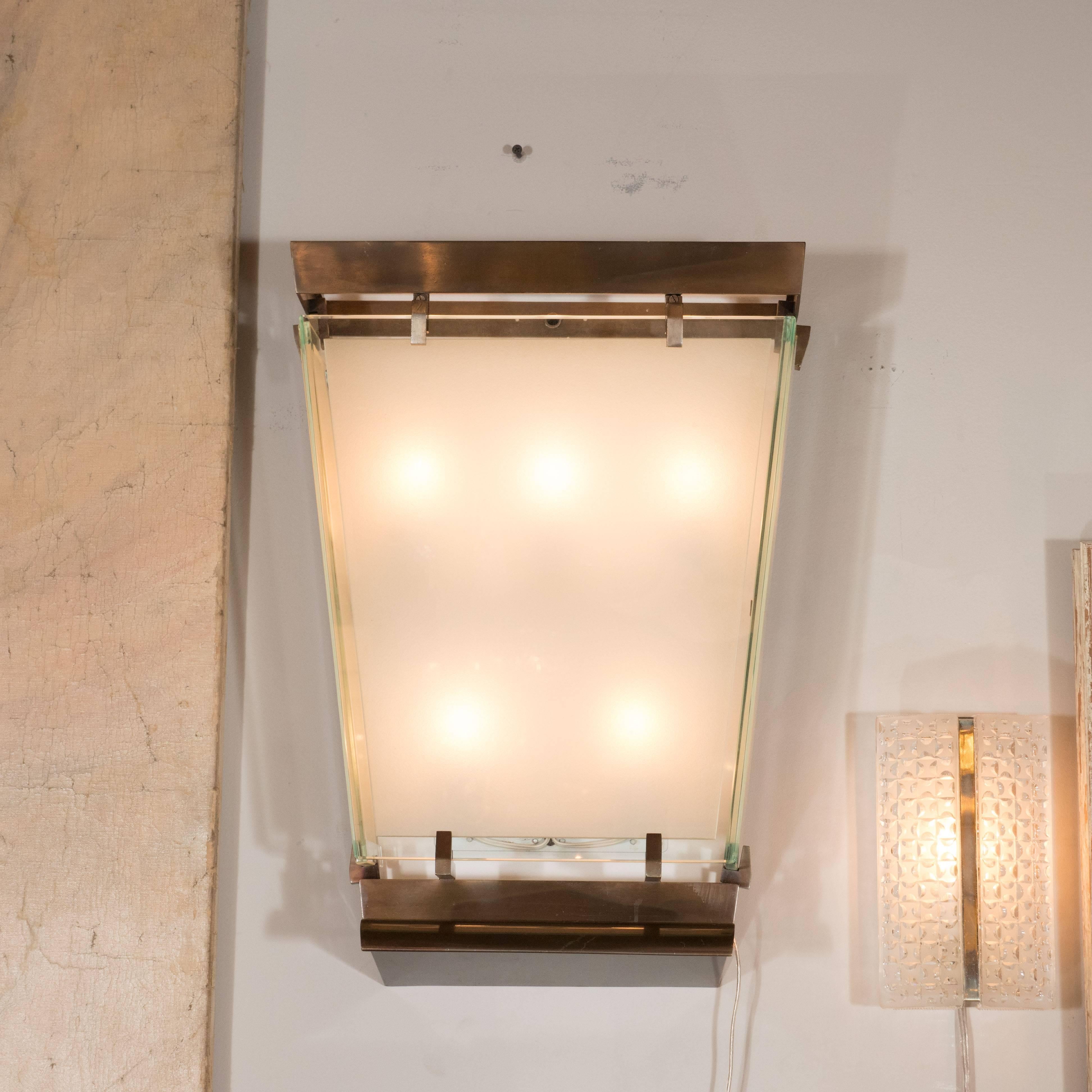 This stunning pair of Art Moderne sconces were realized in France, circa 1950. They feature rectilinear patinated brass frames with L-shaped supports in the same materials. In the center of each sits a frosted glass frame with translucent borders