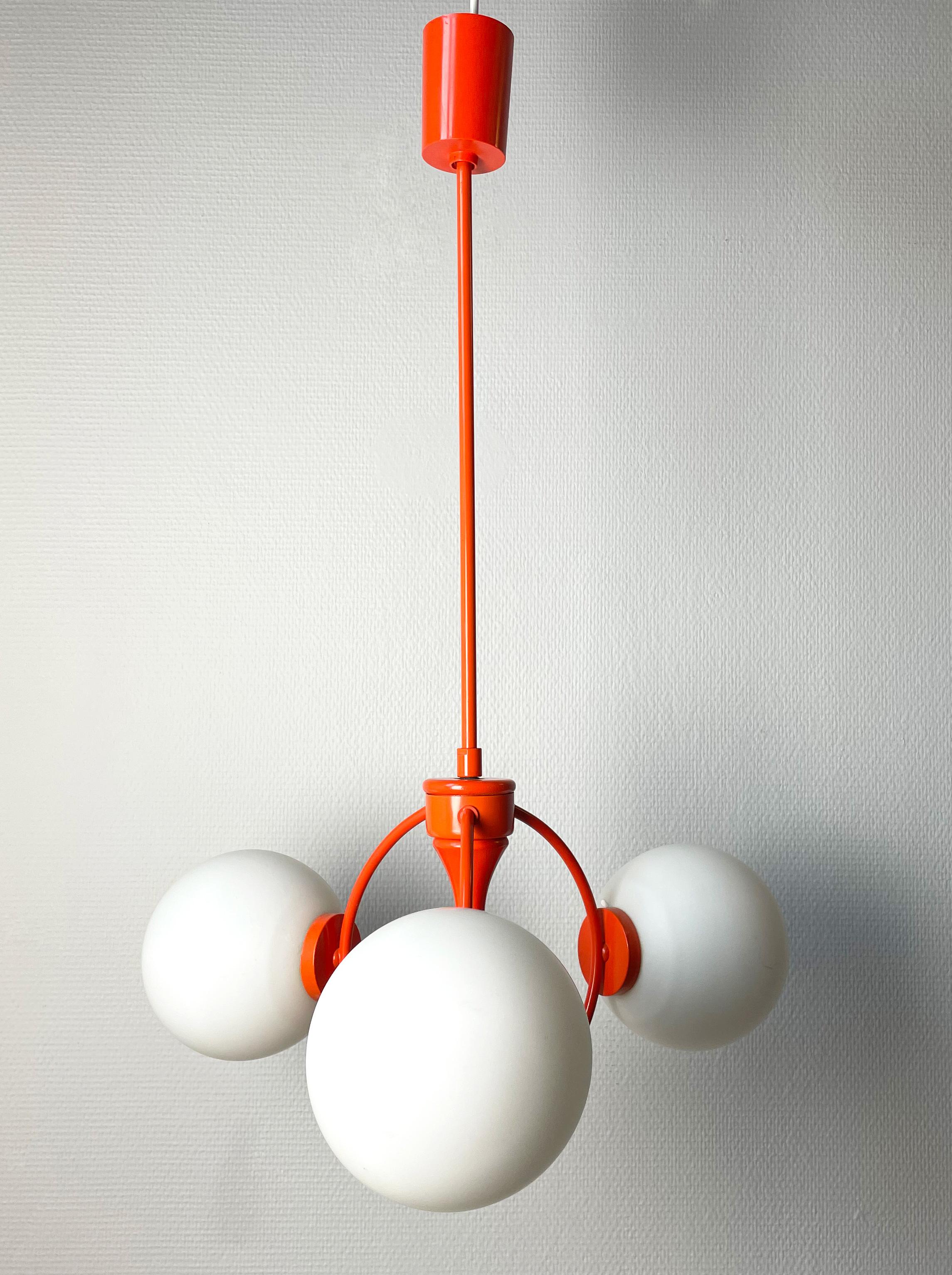 Striking modernist space age Kaiser pendant with three crisp white opaline glass spheres of light. Eyecatching orange molecular metal and wood mount with canopy. Manufactured by Kaiser Lighting in Germany in the 1960s. Three sockets for E14 40W