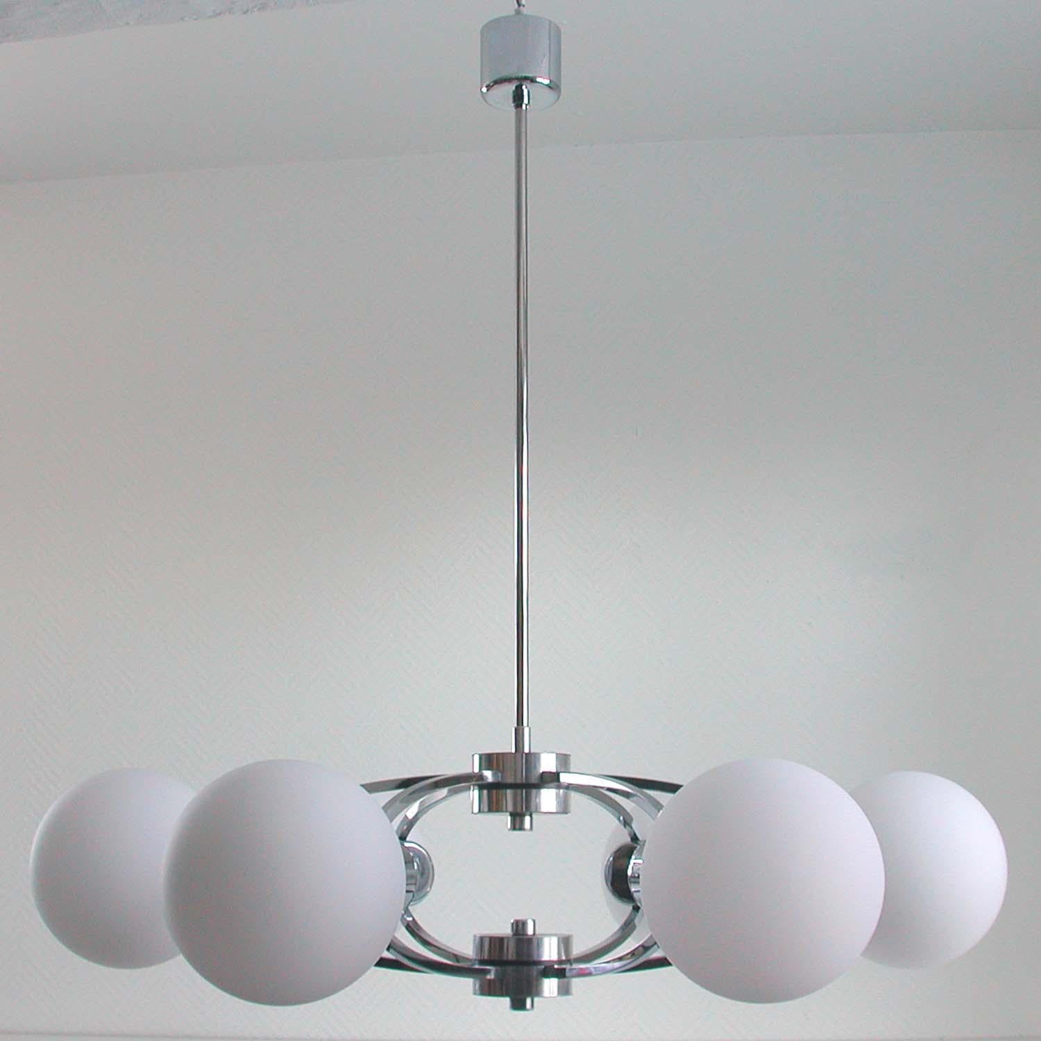 This beautiful chandelier was designed and manufactured in Germany in the 1960s. It is made of chrome-plated metal and has got six white frosted satinated glass lamp shades. Each lamp shade has got a E14 screw on socket. Diameter of each shade is