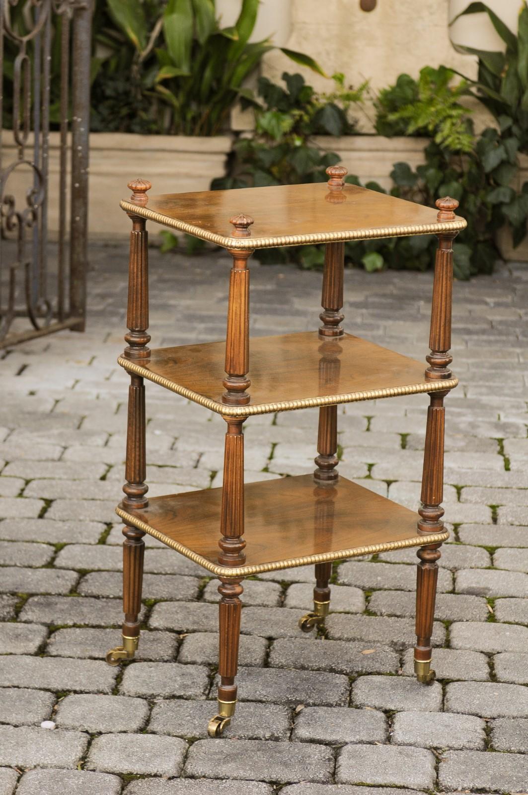 A Vintage mahogany étagère on brass casters by Baker Furniture from the mid-20th century with three shelves, gilded gadrooned motifs and reeded legs. Born during the midcentury period, this elegant étagère features three rectangular shelves, each