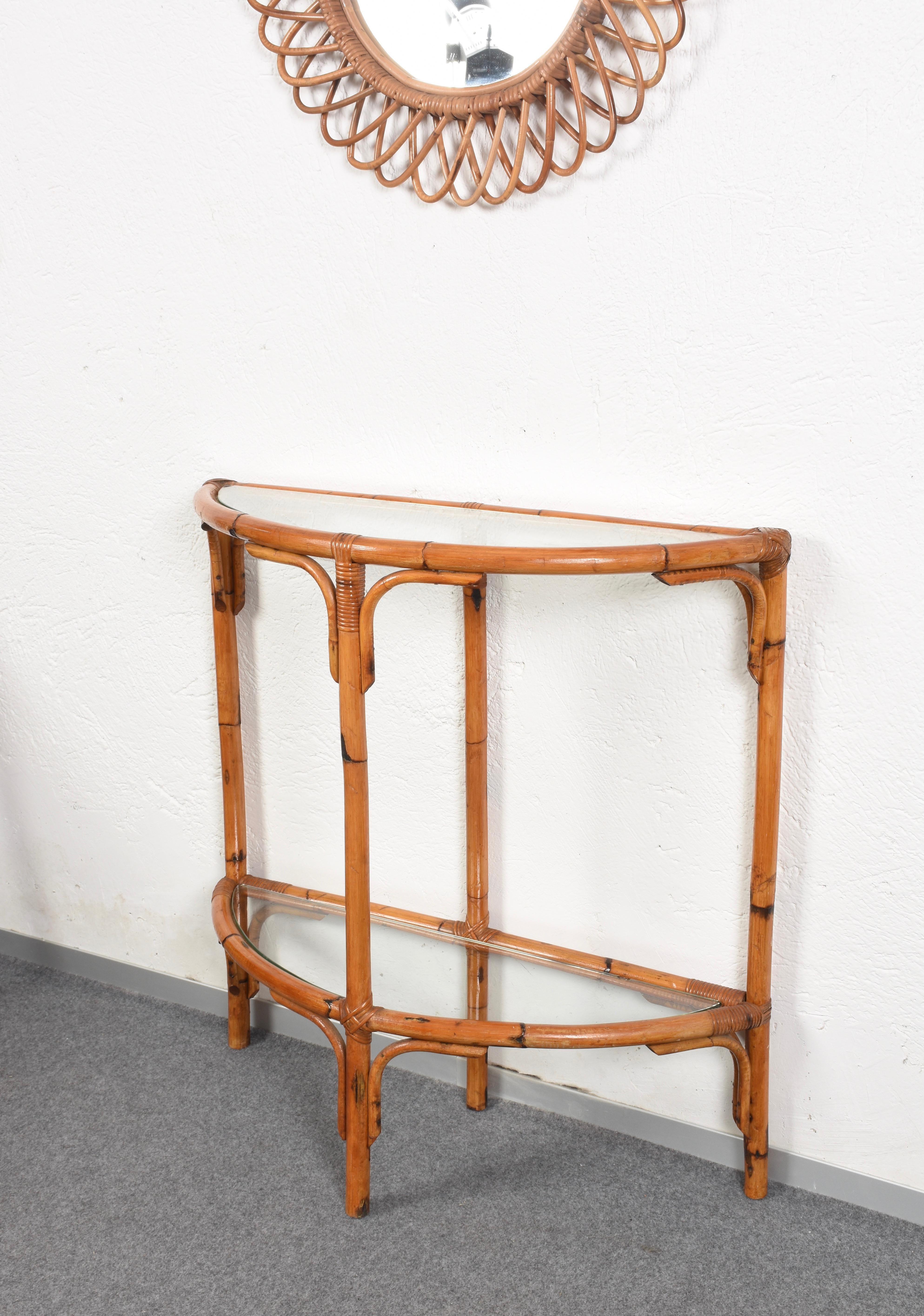 Eye-catching bamboo and rattan arched console table with two half-moon glass shelves. This piece was produced following the style of Franco Albini in Italy during 1970s.

This console table stands upon three bamboo legs joined between them by a