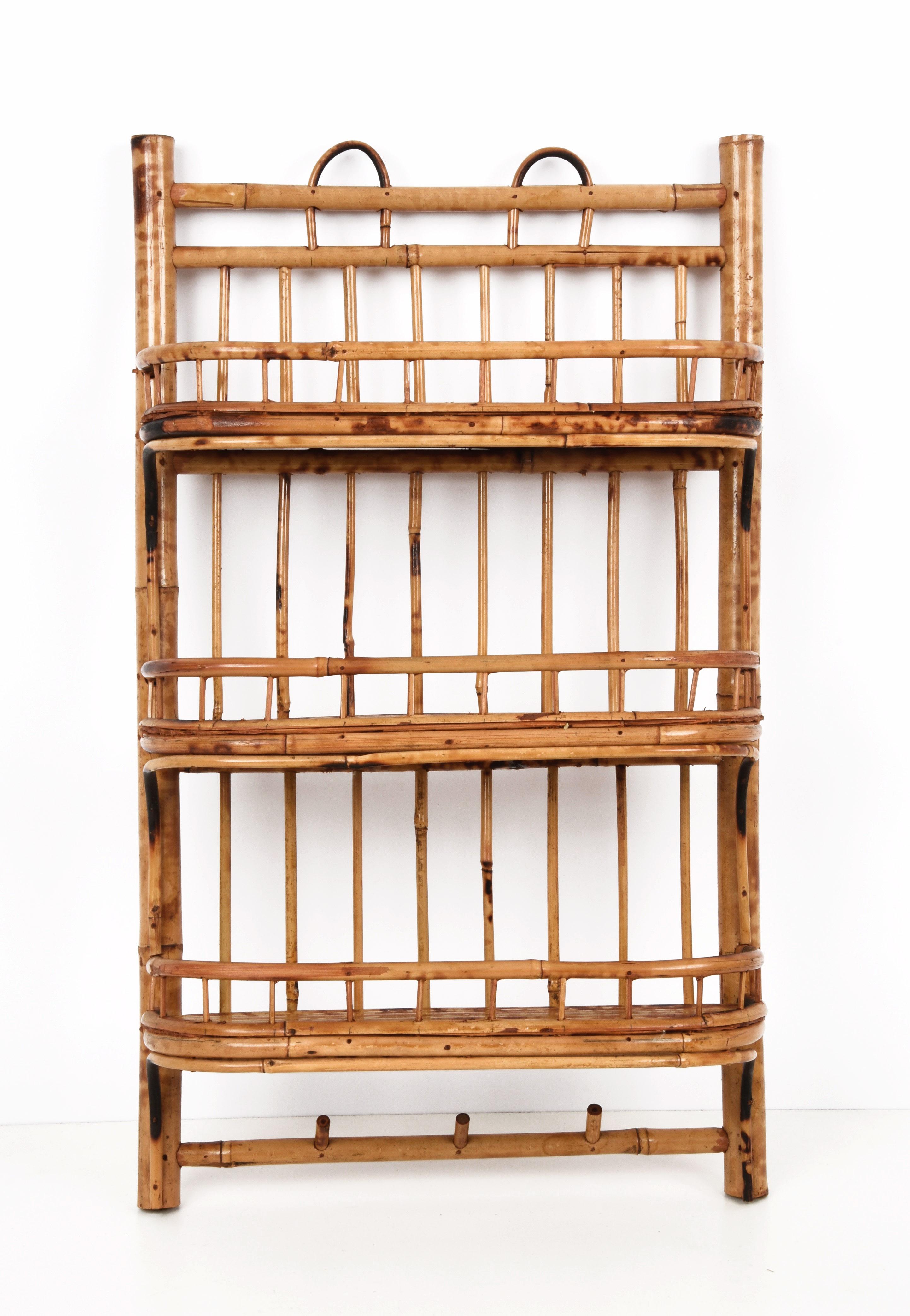 Amazing mid-century bamboo and rattan shelf or hanging side table. This fantastic piece was produced in Italy during the 1960s.

This elegant item is unique in that it has three rattan shelves and three hooks at the bottom.

A multipurpose and