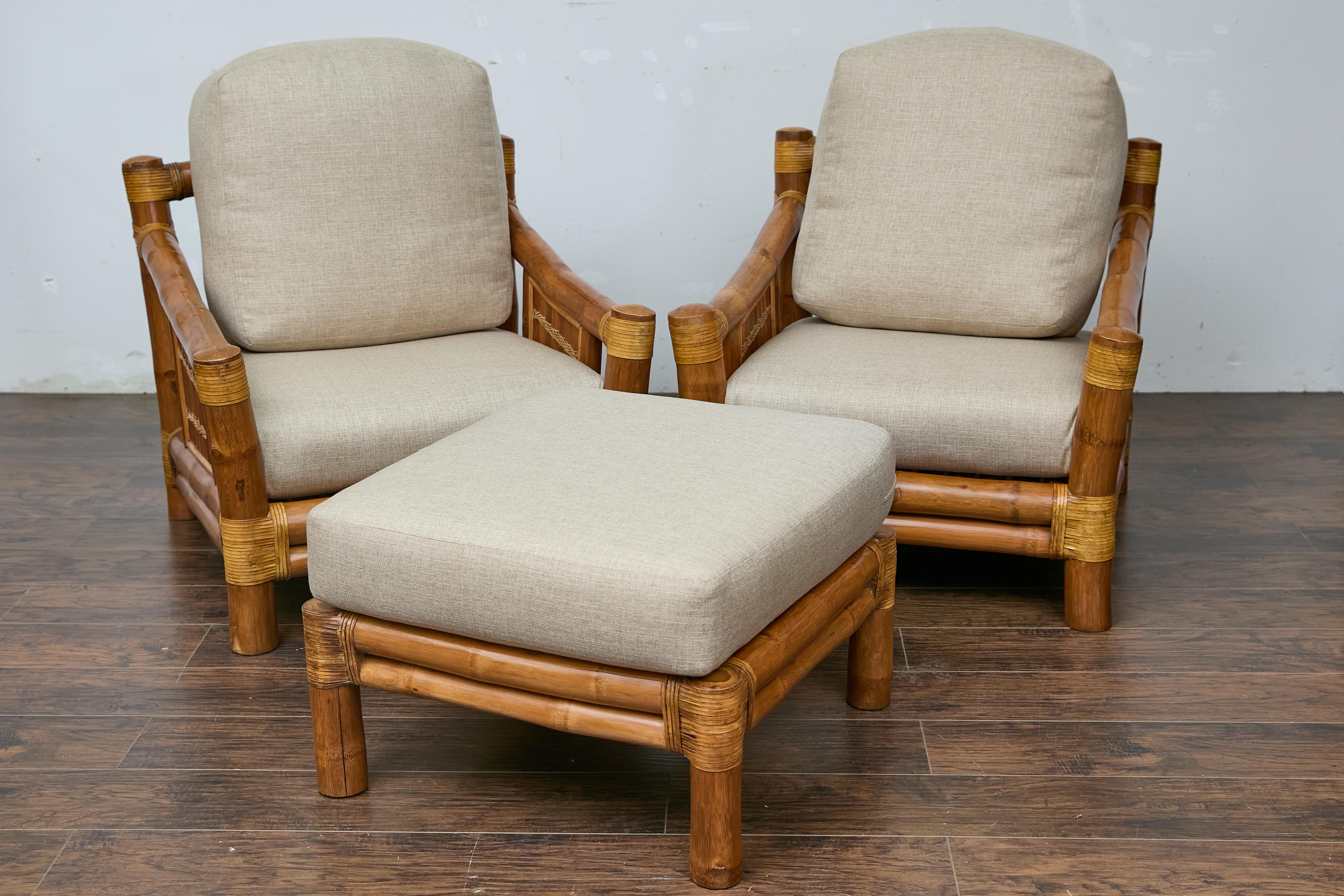 A set of two bamboo lounge chairs with their ottoman from the Midcentury period, with rattan accents and custom linen upholstery. This charming set of two Midcentury bamboo lounge chairs with their matching ottoman captures the essence of organic