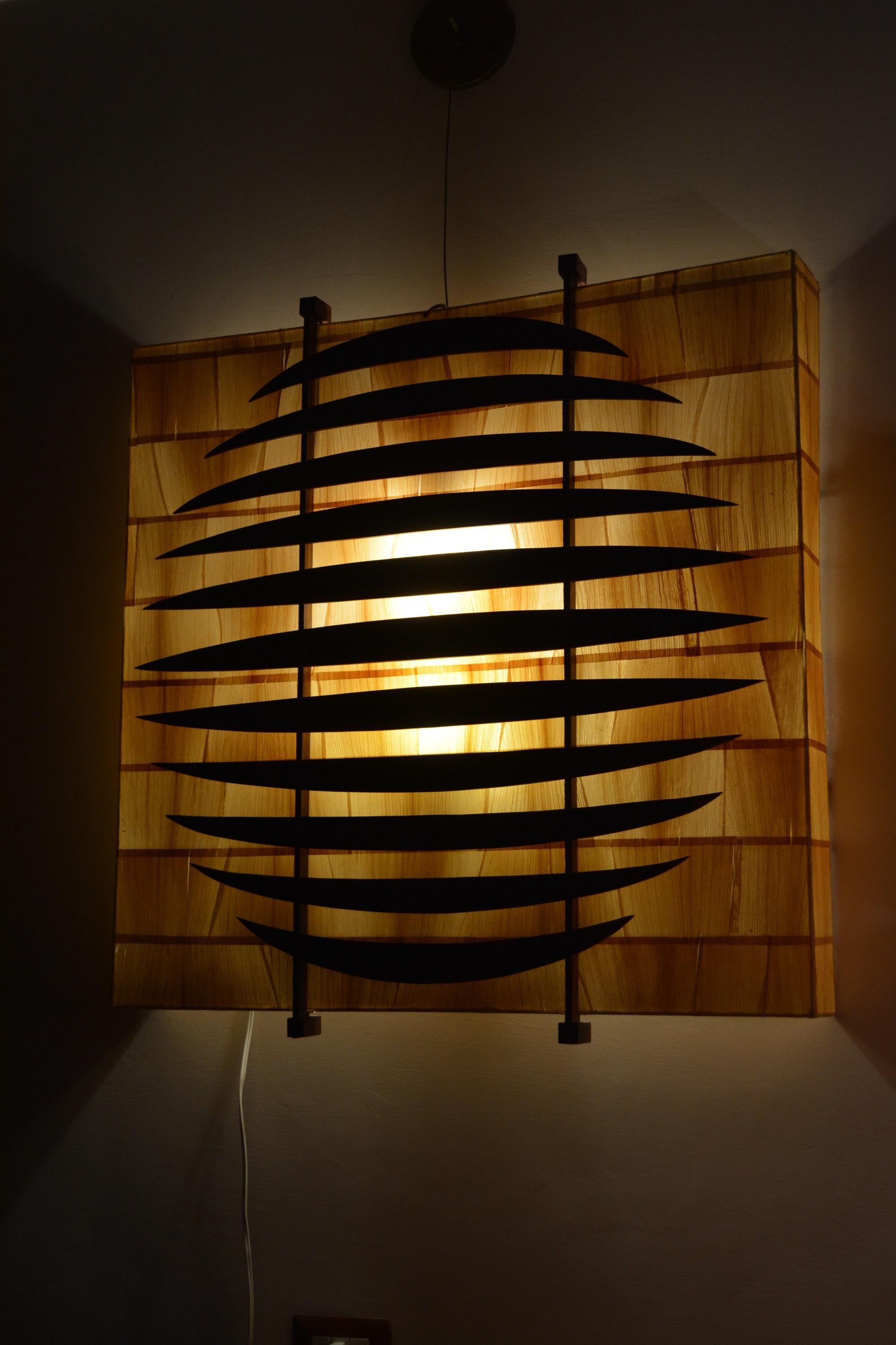 Wall lamp of dry banana leaves glue on a carbonate and metal support, the structure decorated with teak wood.
Not signed.
Made on 1970-1980
Dimension 78 x 78 x 10 cm. 

 