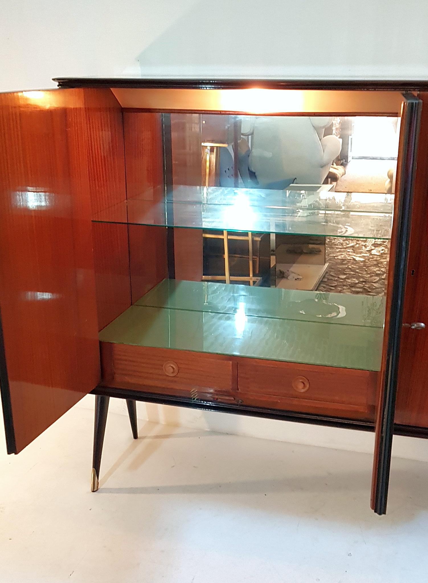 Midcentury bar cabinet produced in Italy in the 1950s. The base is made from stained beech and the legs has brass caps. The cabinet is made in jacaranda and has panels in poplar root and finally the top is made from glass which has a green/turqoise