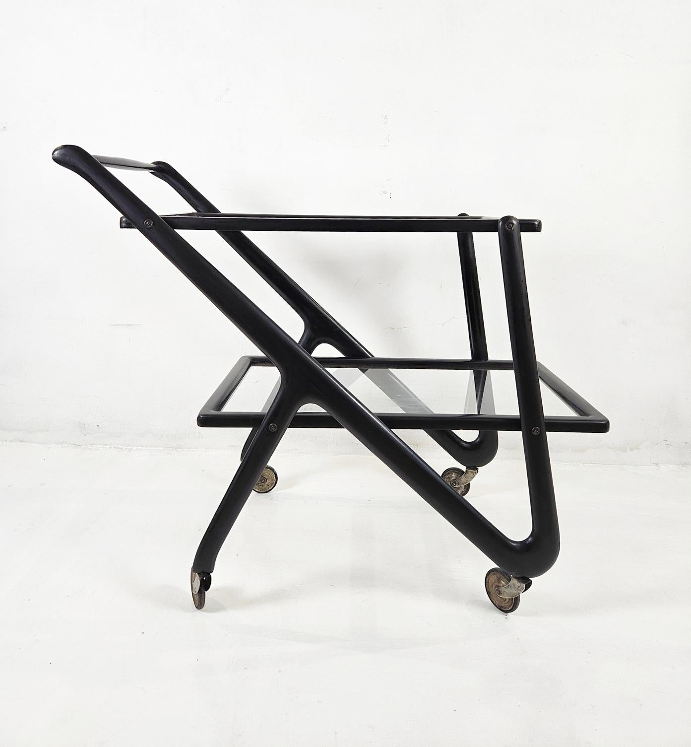 An original two tiered midcentury bar cart by Cesare Lacca, Italy. Made in stained lacquered beech in a design typical for Lacca. Featuring wo tiers in clear glass surrounded by stained beech wood. The castors are also original and in good working