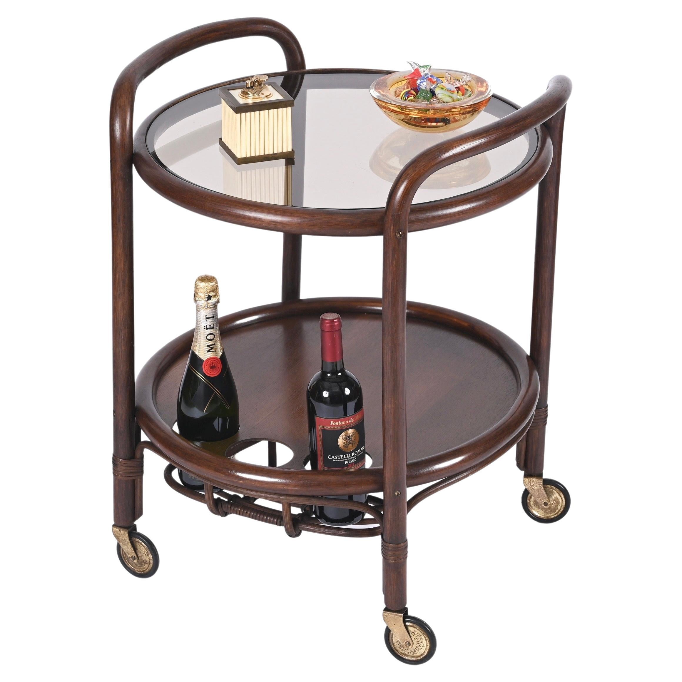 Gorgeous midcentury round serving cart in bamboo, rattan, walnut wood and smoked glass top with brass wheels. This stunning piece was produced in Italy in the 1970s.

The bar cart features a structure fully made in bamboo with two stunning tiers
